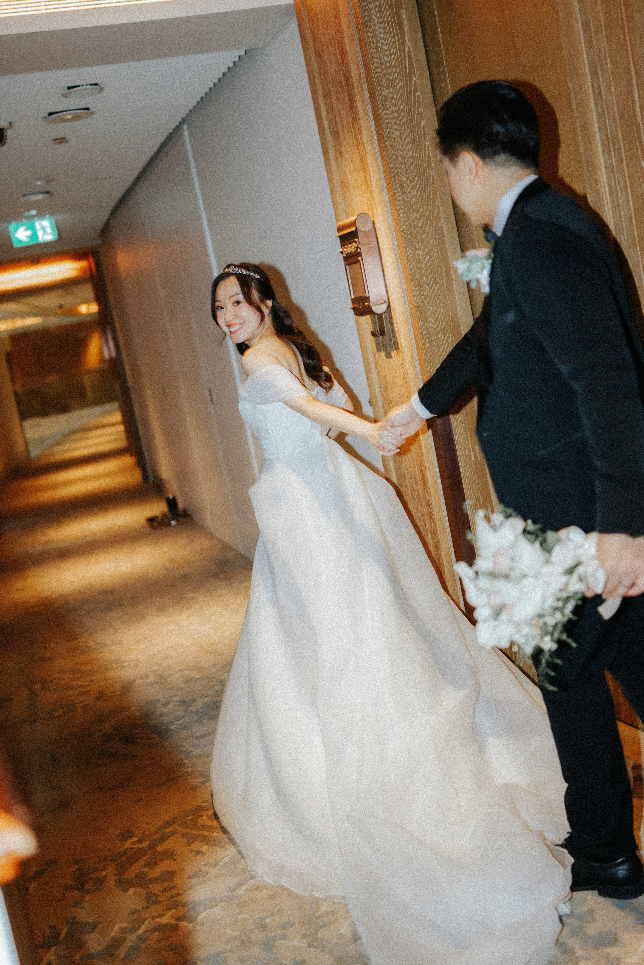 Cinematic actual day wedding photoshoot of a bride leading her groom through a corridor towards their wedding, captured by Breadandbutterworks in a soft and heartfelt style.
