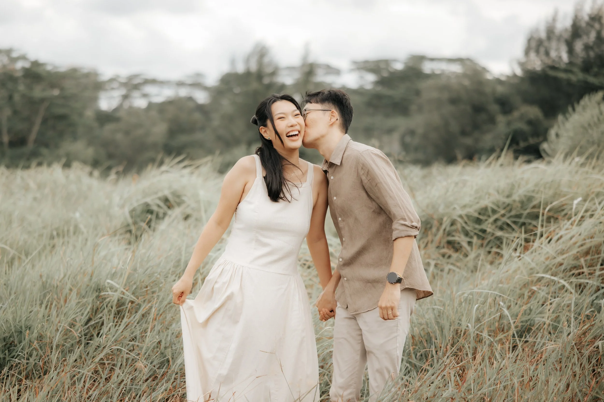 Playful pre-wedding photo of a couple posing among the tall grass at East Coast Park, captured by Breadandbutterworks in a soft and heartfelt style.