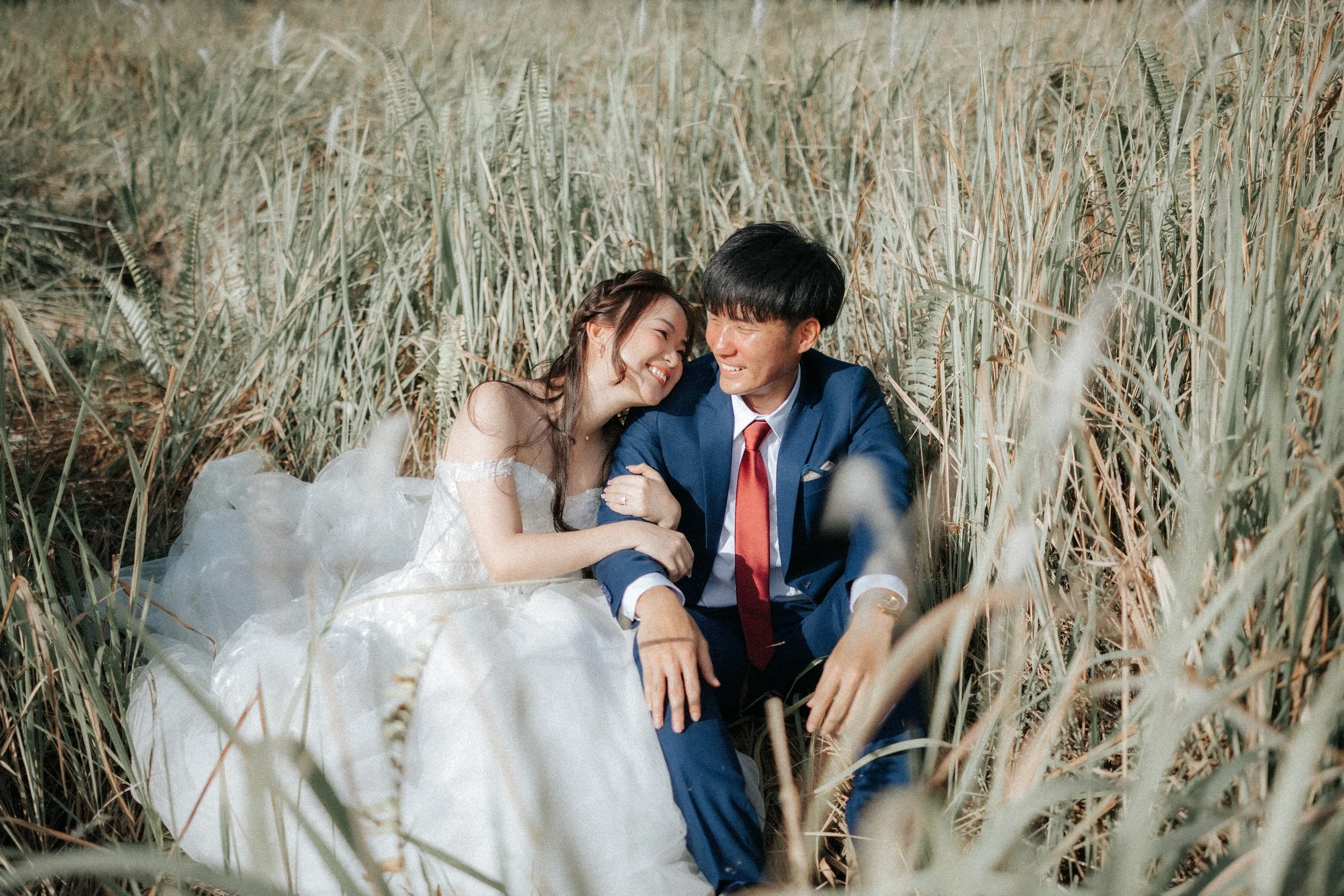 Romantic pre-wedding photo of a couple sharing a moment in the tall grass of Jurong Lake Gardens, with the bride cuddling up against the groom in Singapore.