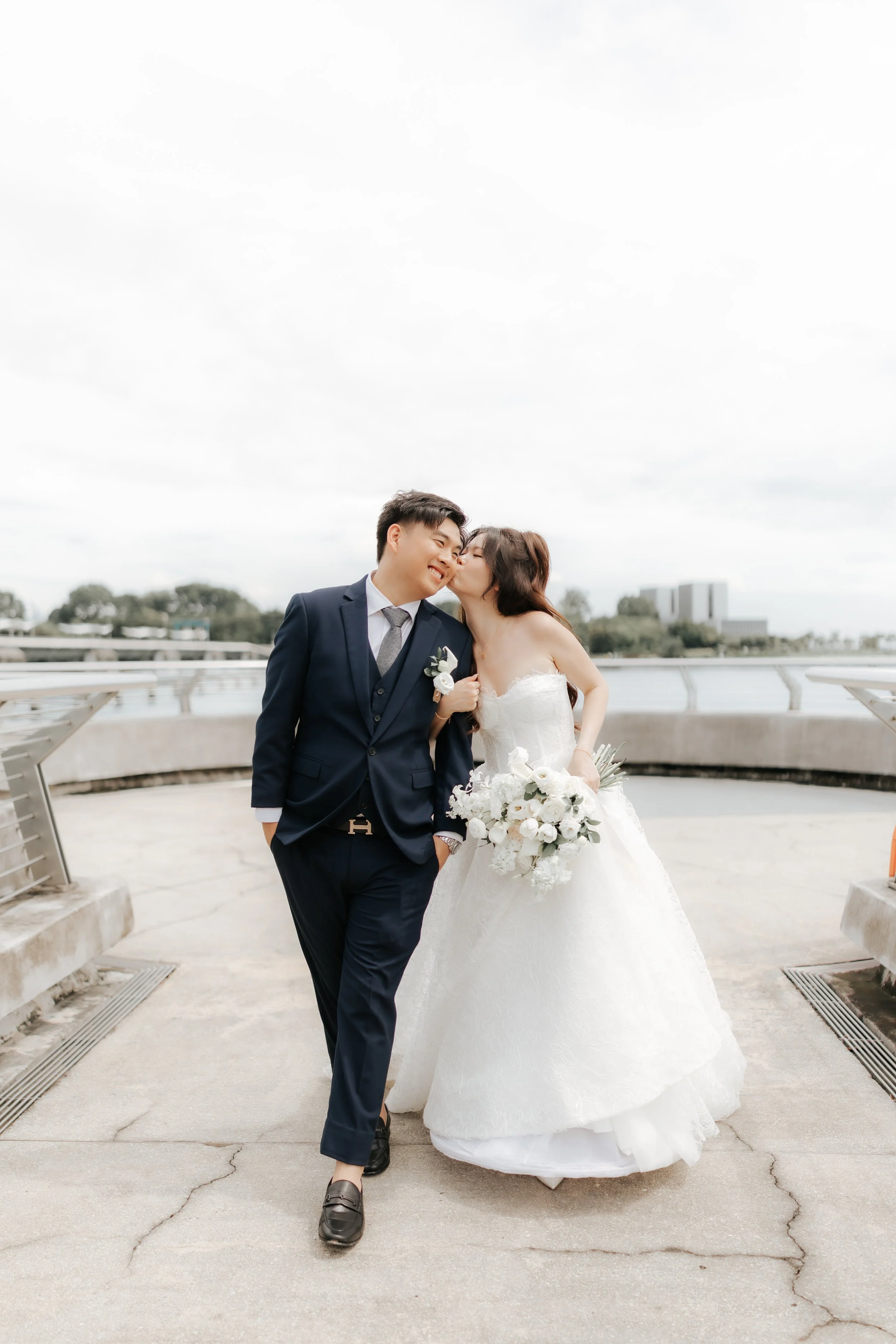 Cute actual day wedding couple's photo of the bride and groom walking along Marina Barrage, captured by Breadandbutterworks in a soft and heartfelt style.