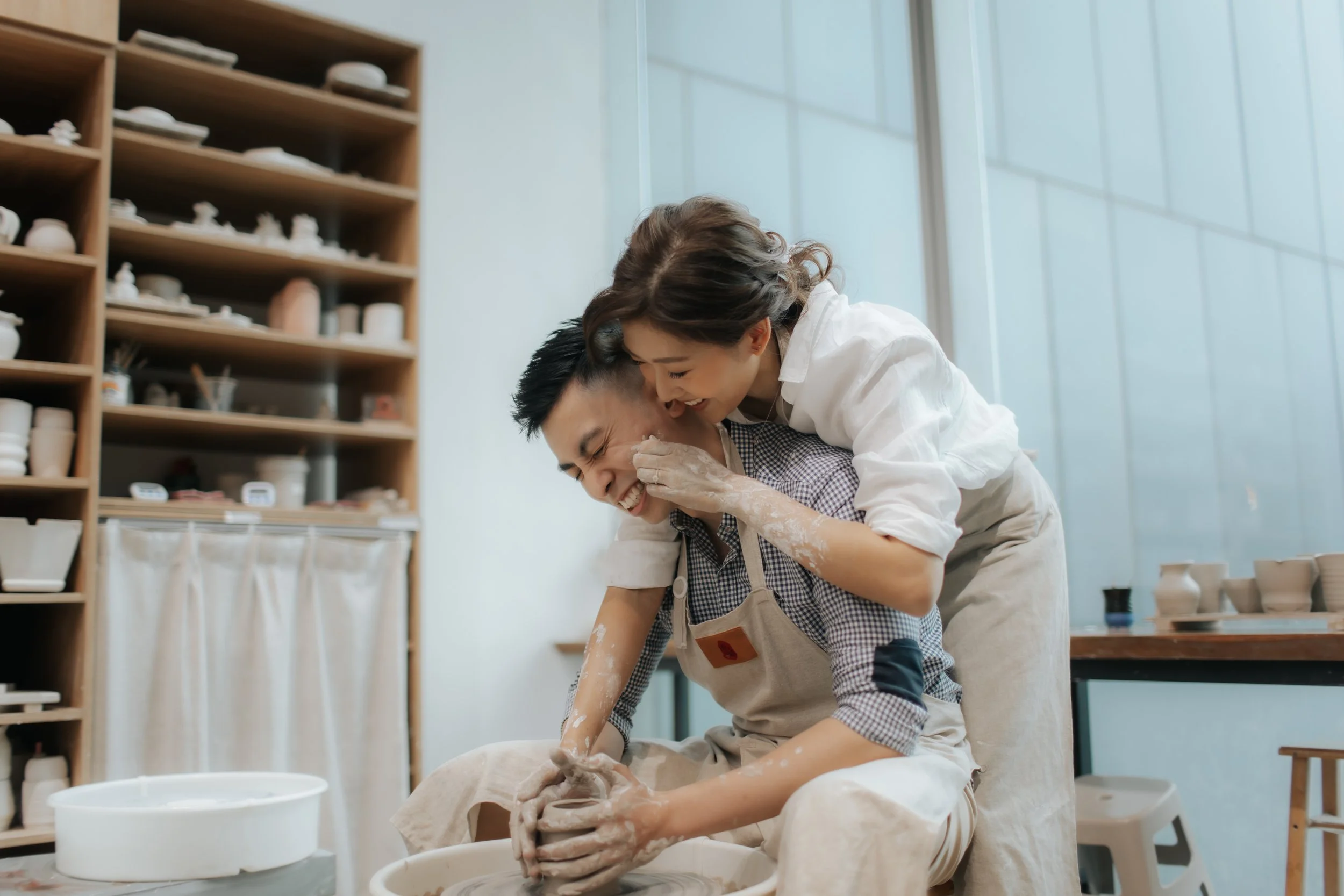 Intimate pre-wedding photoshoot at a pottery studio in Singapore (Tao Pottery), the couple is working on a pottery wheel in a romantic fashion. Captured in the light and airy style of Breadandbutterworks.