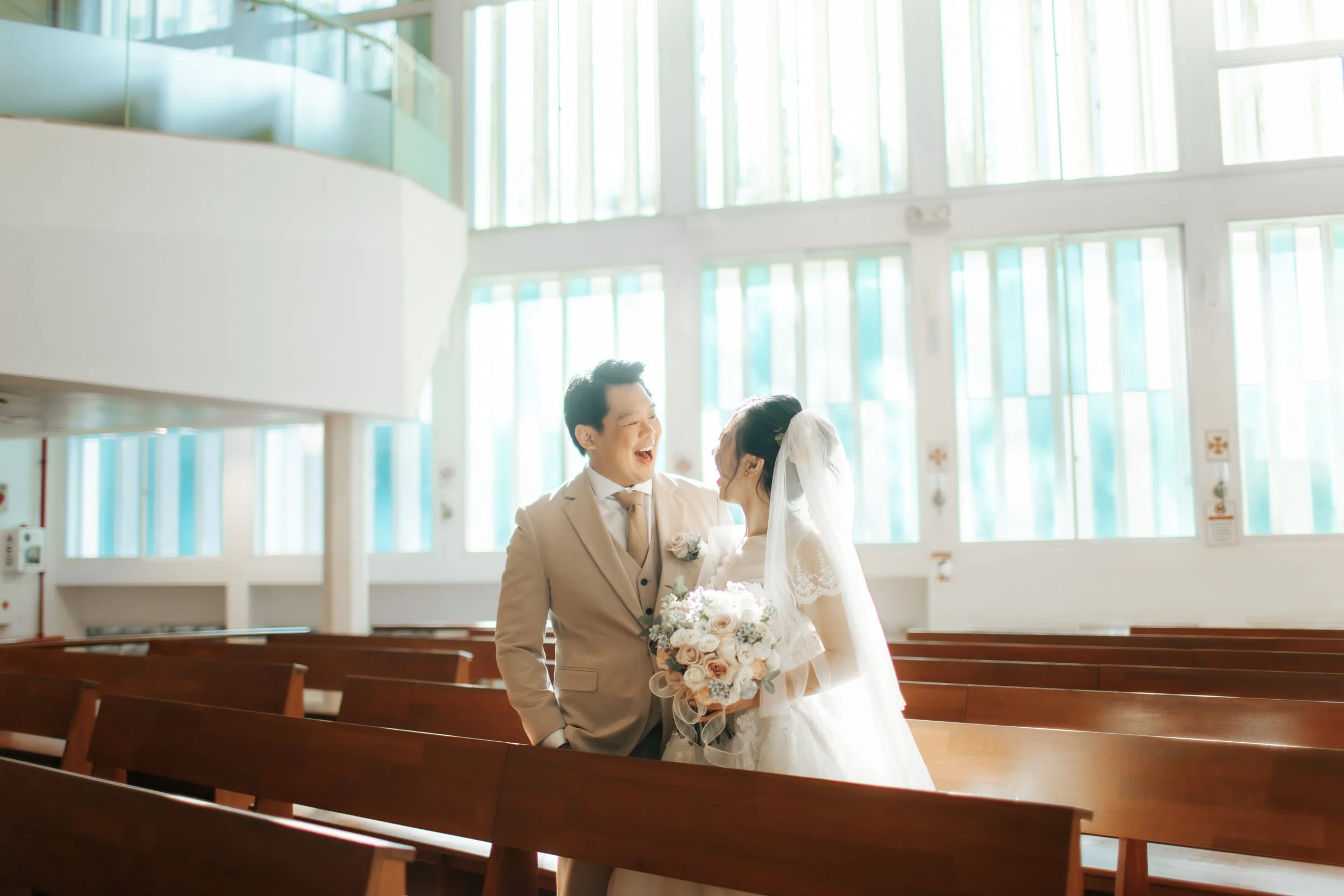 Light and airy actual day wedding photoshoot taken in a Catholic Church of the couple sharing a laugh as they stand excitedly waiting for their big day to commence. Captured by Arielle for Breadandbutterworks. 