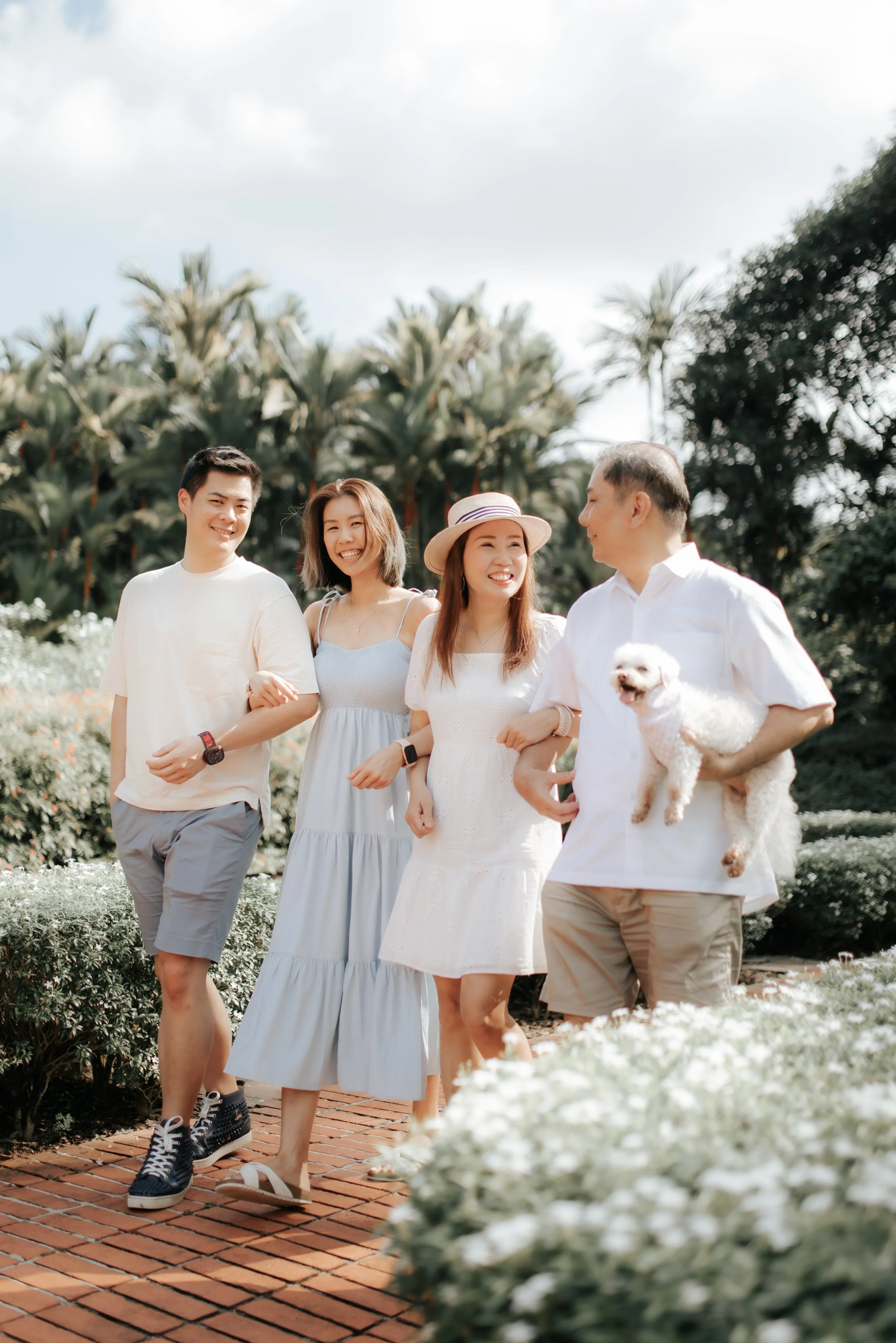 Light and airy family photoshoot in Singapore featuring a family strolling through a park outdoors with their pet dog, captured by Breadandbutterworks.