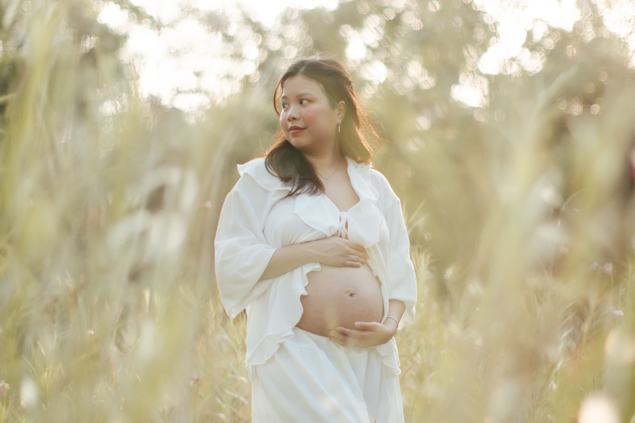 Light and airy maternity shoot at bandstand, the mother-to-be poses within a field of long grass, captured by Arielle for Breadandbutterworks.