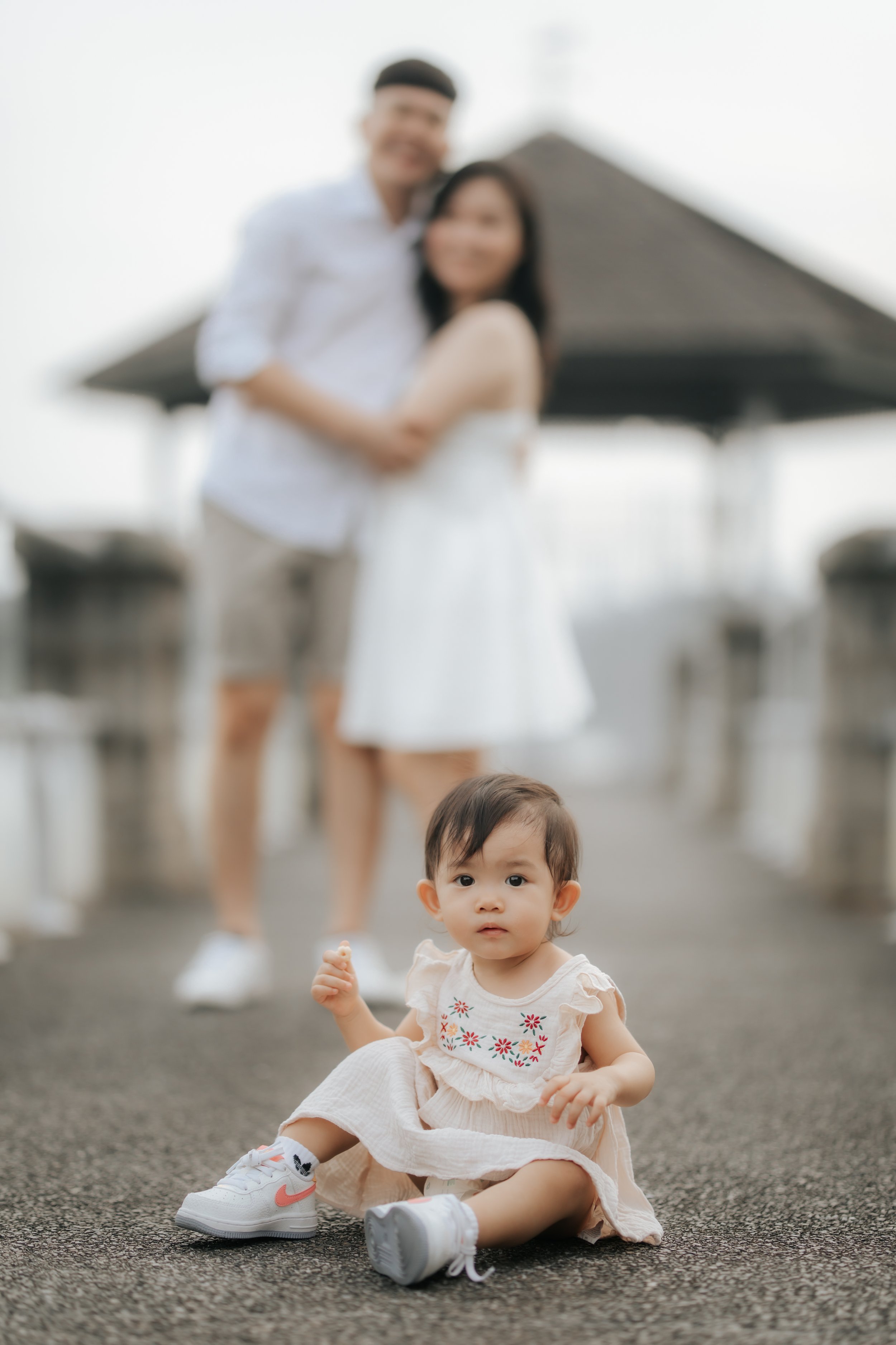 Light and airy creative bokeh family photo of a young family on a bridge, captured in a soft outdoor setting in Singapore.