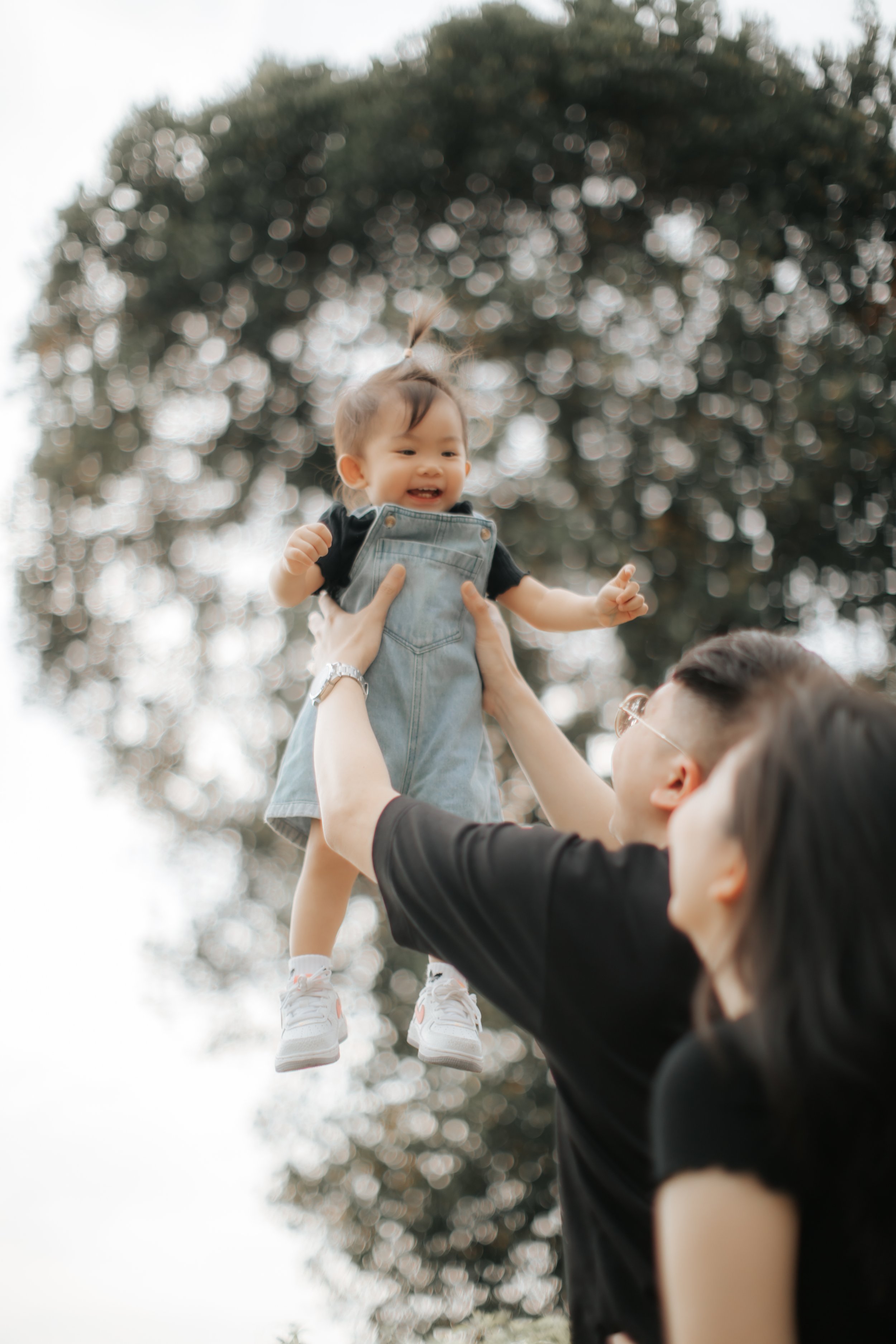 Light and airy family photo of a young family playing with their baby, captured in a soft outdoor setting in Singapore.