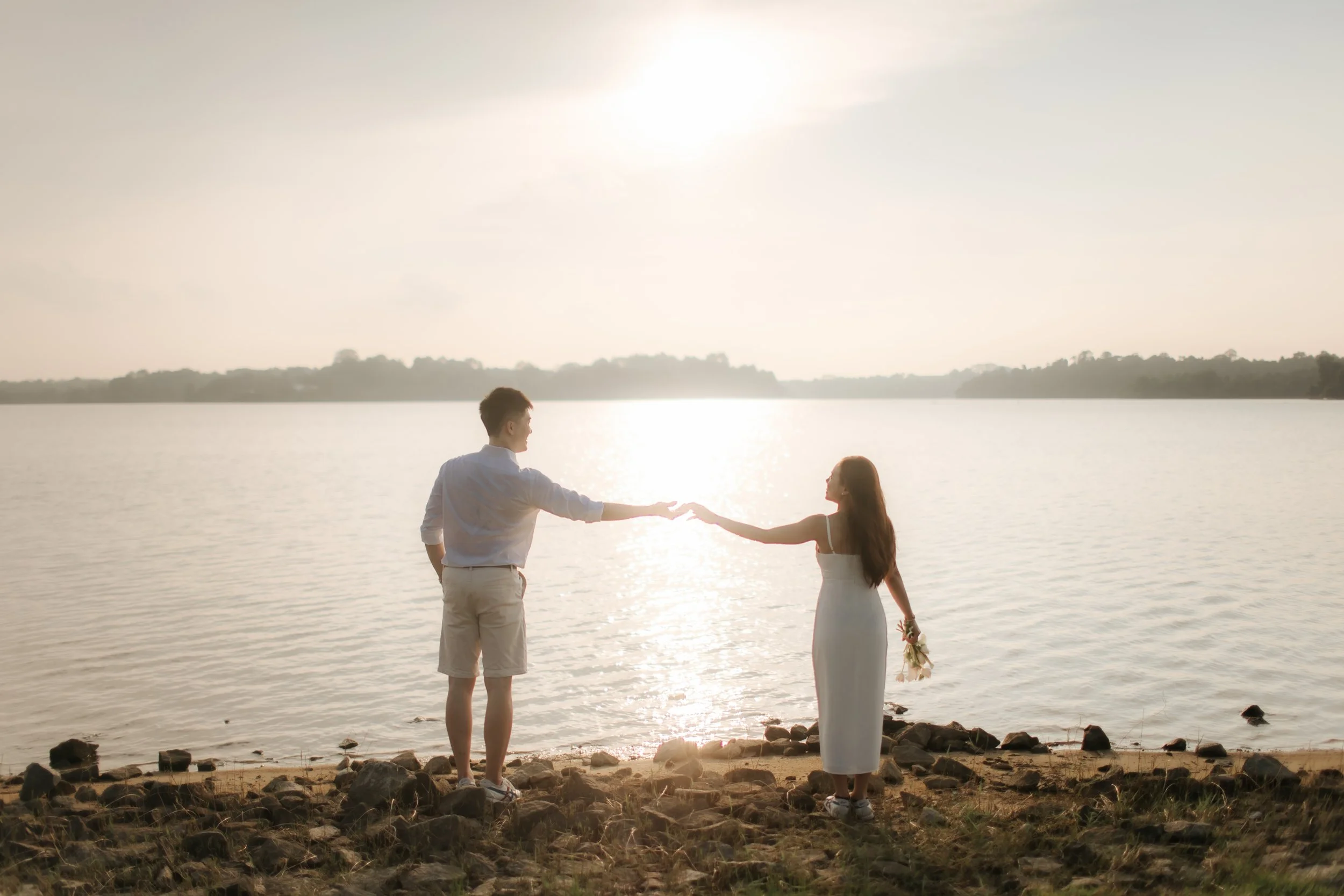 Romantic and airy pre-wedding photoshoot at Upper Seletar Reservoir, the couple is enjoying the view of the setting sun bouncing off the water. Captured by Arielle from Breadandbutterworks.
