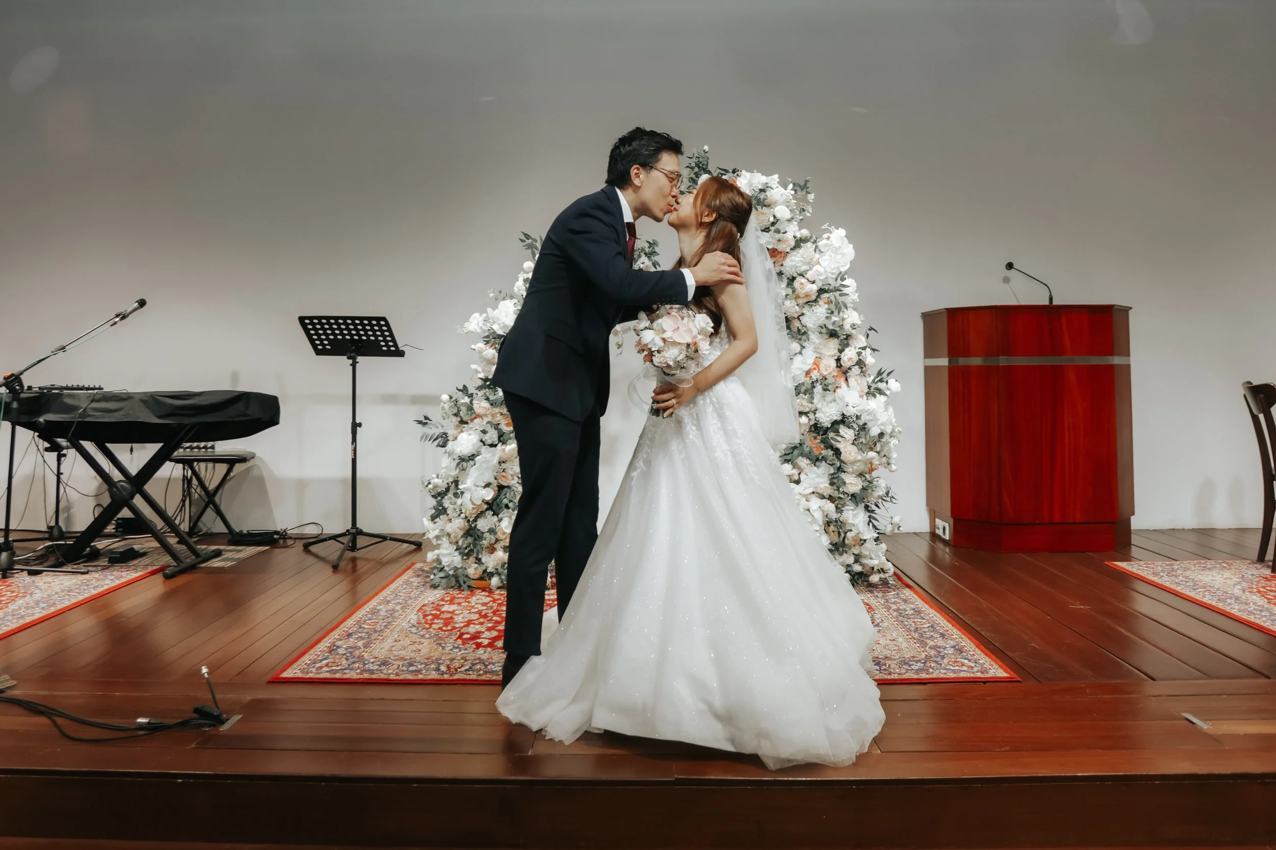Light and airy actual day photoshoot of a couple on stage at Bukit Panjang Church, they share a kiss after being pronounced husband and wife. Captured by Arielle for Breadandbutterworks.