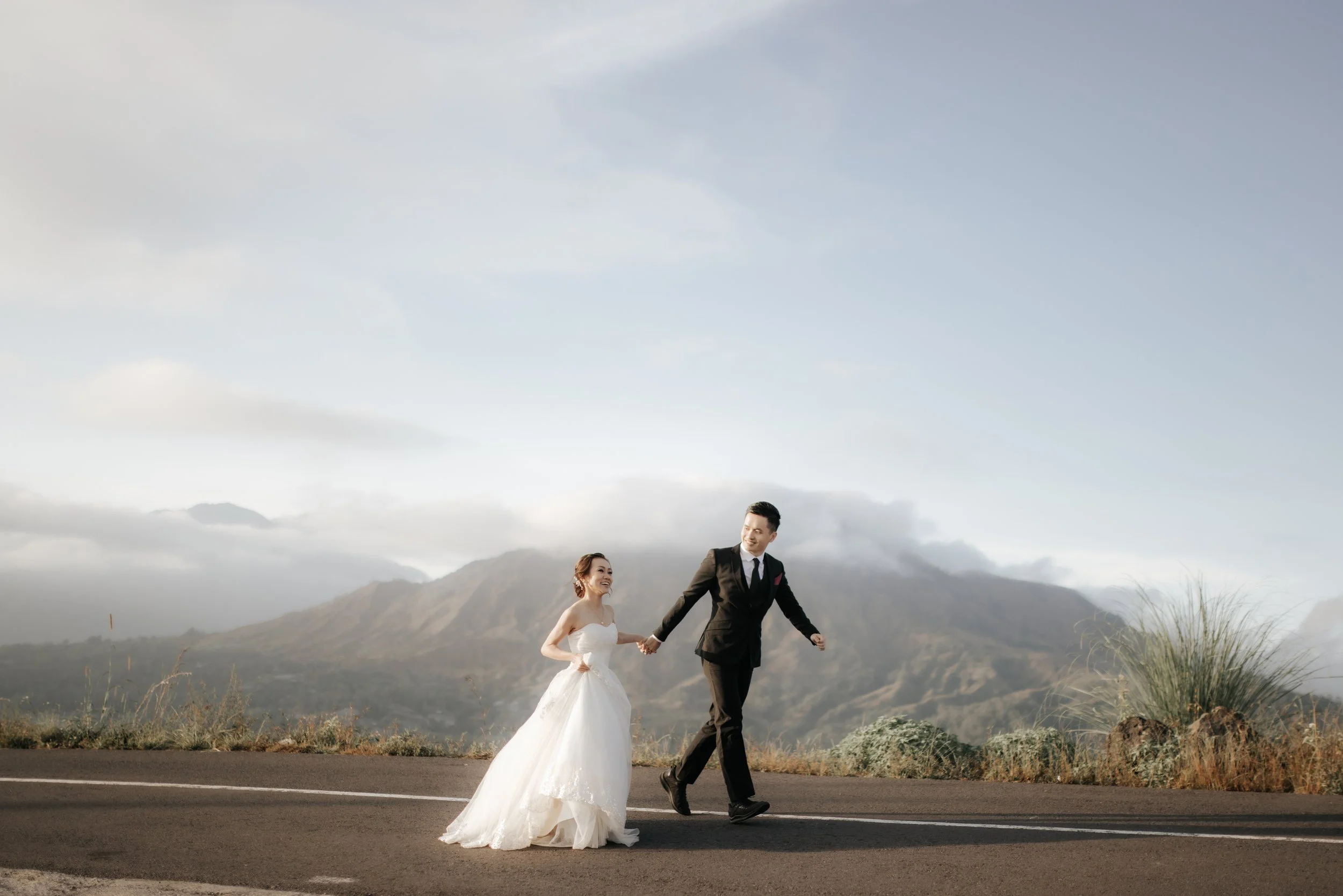 Cover image for Ash’s overseas pre-wedding photography collection, featuring a couple walking together against a mountain backdrop in Bali.