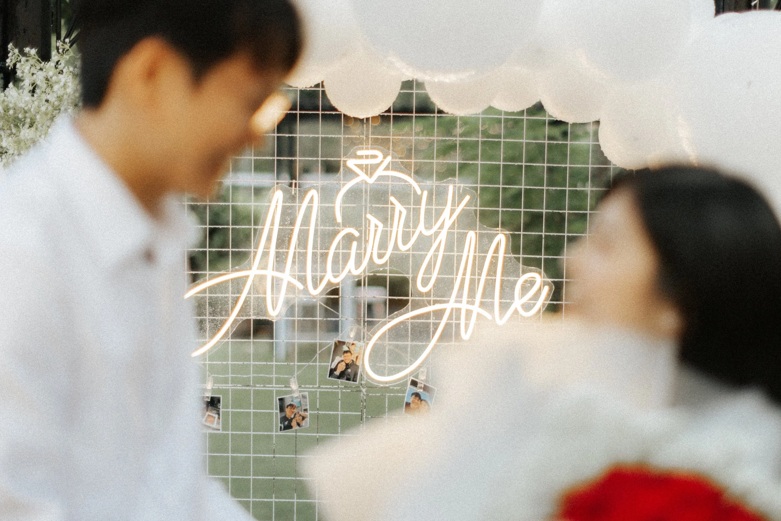 Proposal photography in Singapore featuring a glowing “Marry Me” sign with the couple softly blurred in the foreground, captured by Breadandbutterworks.