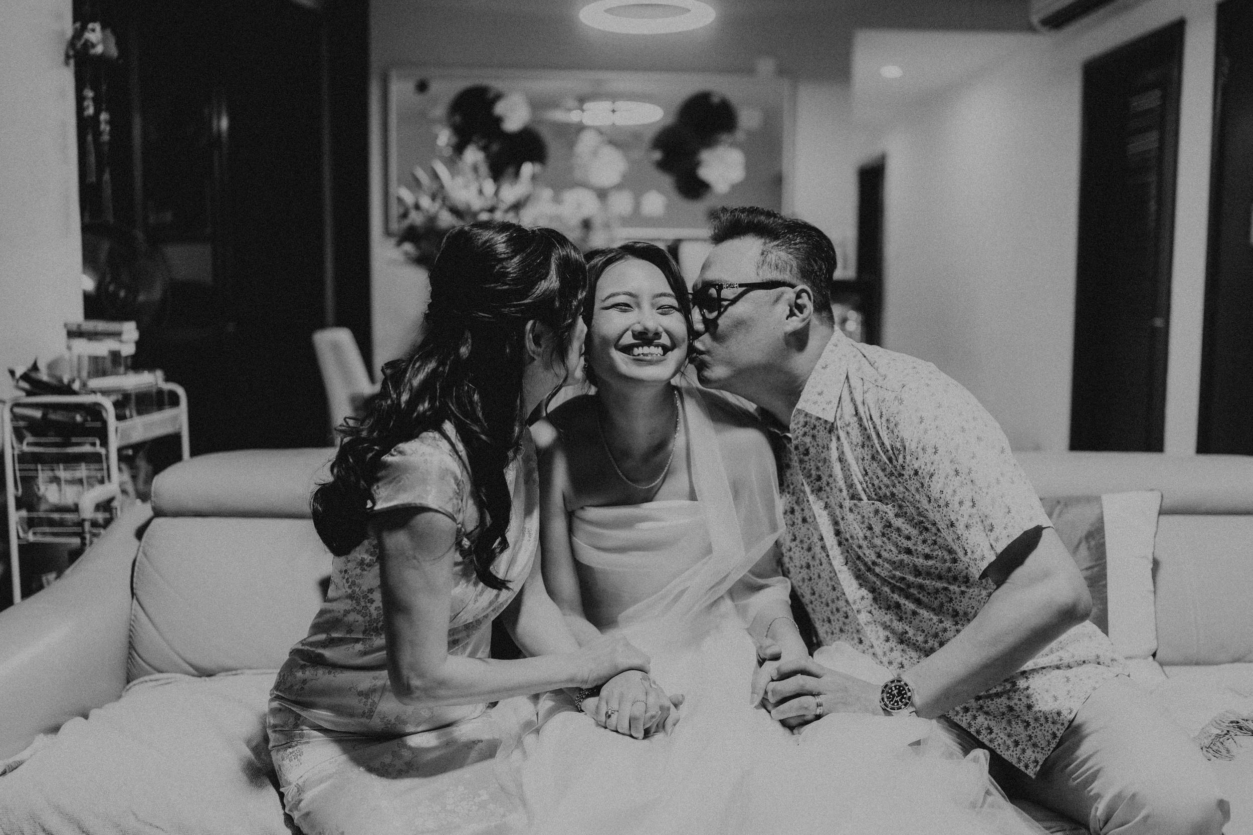 Joyful actual day wedding photography of the bride-to-be getting kissed by her parents as they veil her, captured by Breadandbutterworks in a soft and heartfelt style.