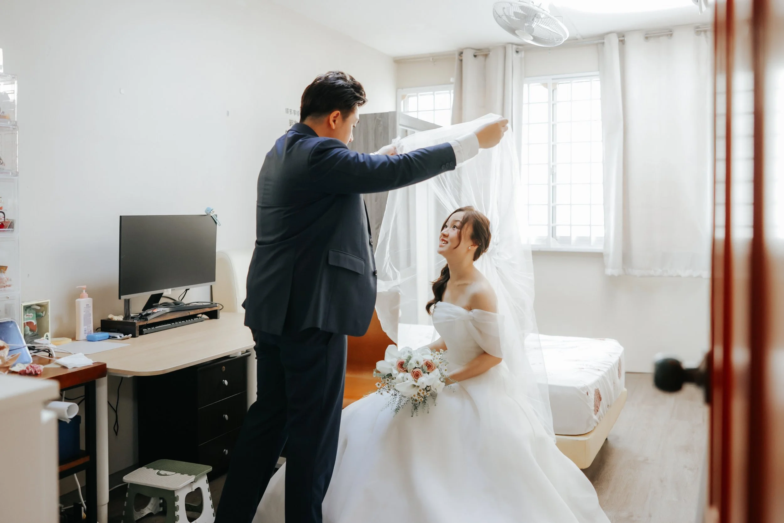 Joyful actual day wedding photo of a couple's first look at each other as the groom lifts the bride's veil at her home. Captured by Breadandbutterworks in a soft and heartfelt style.