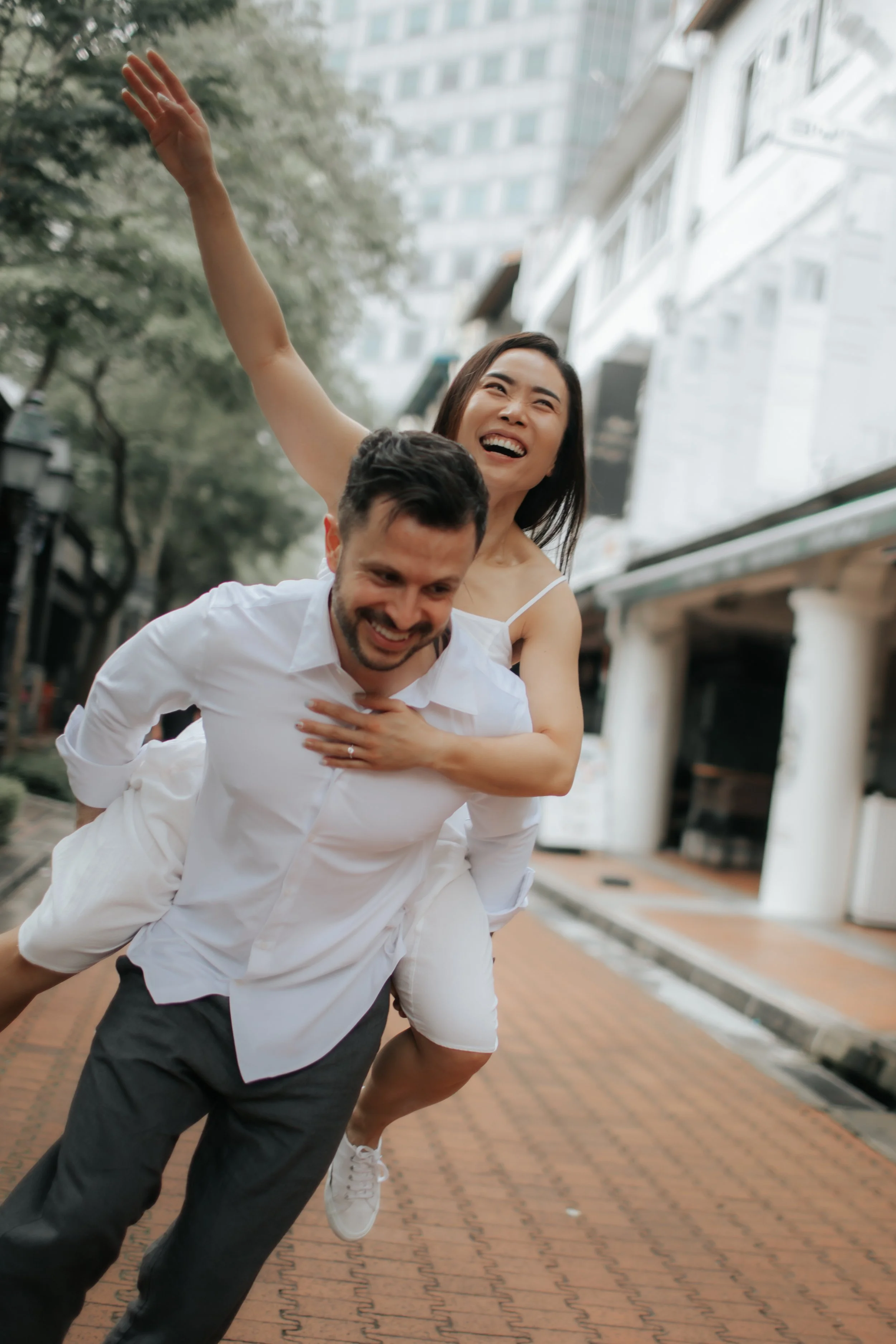 Light and airy proposal photoshoot at Anderson Bridge, the couple playfully poses with the groom-to-be piggy backing his fiance. Captured by Arielle for Breadandbutterworks.