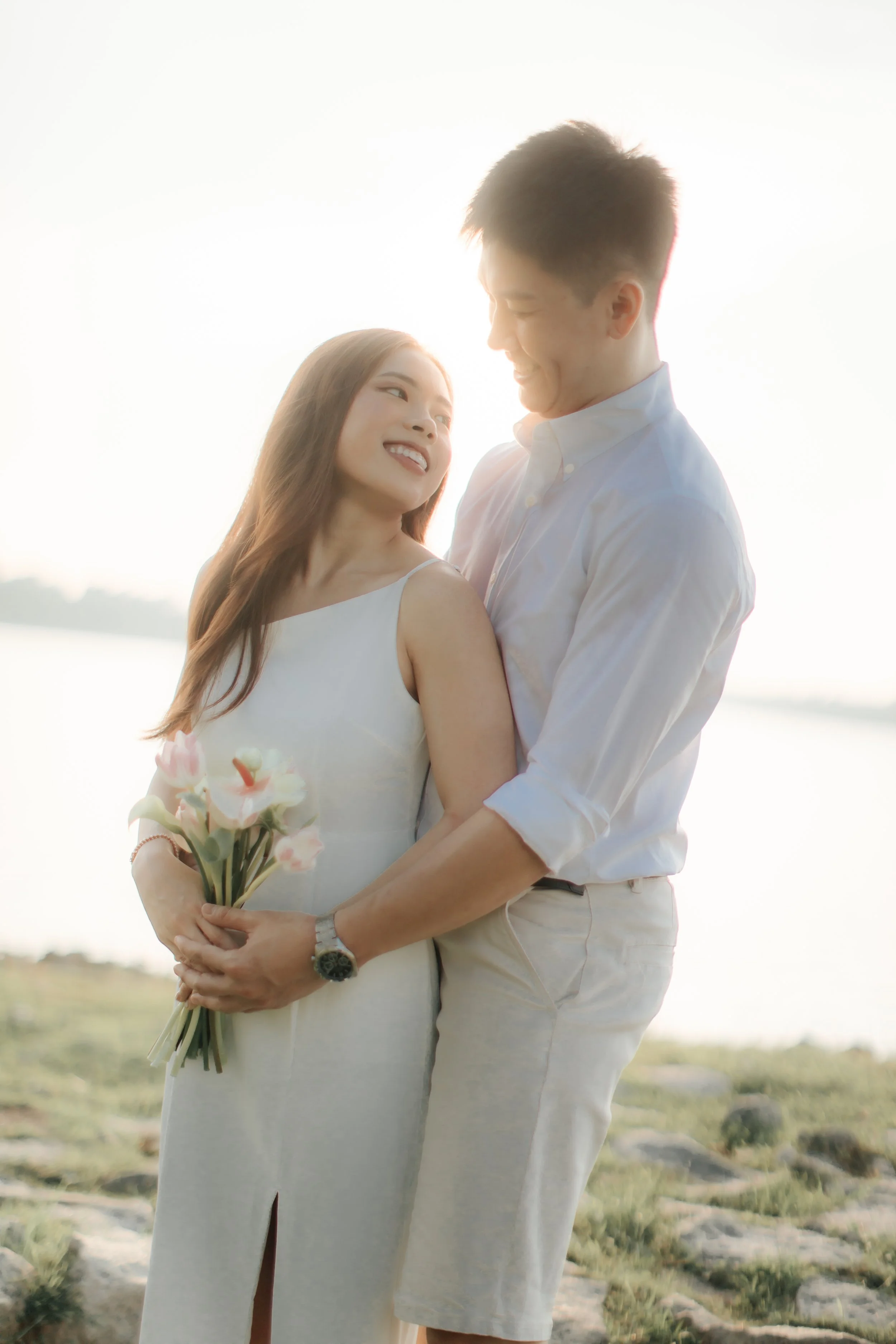 Romantic and airy pre-wedding photoshoot at Upper Seletar Reservoir, the couple is hugging in this intimate shot with the sunset in the background. Captured by Arielle from Breadandbutterworks.