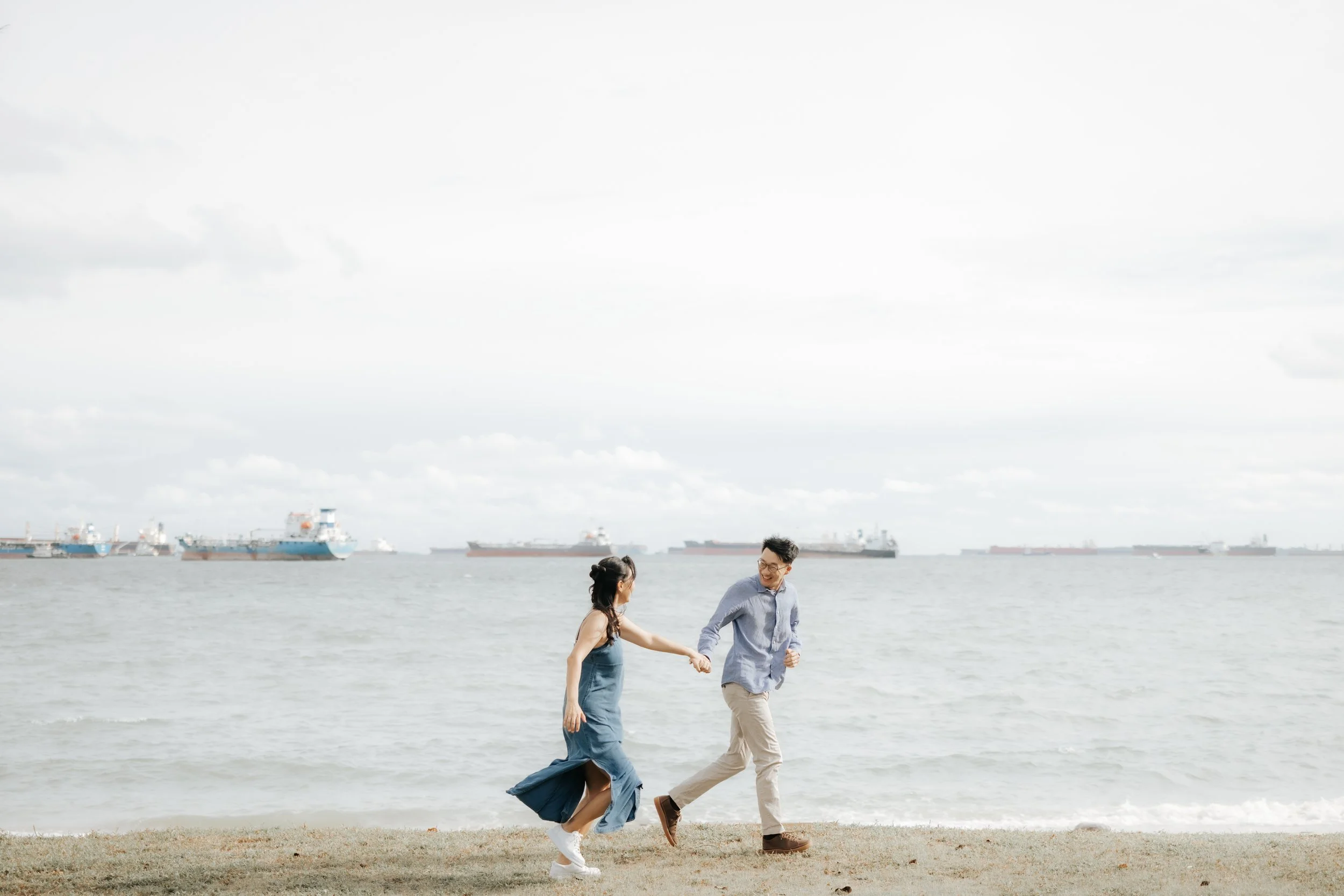 Playful pre-wedding photo of a couple walking hand-in-hand along the coastline of East Coast Park, captured by Breadandbutterworks in a soft and heartfelt style.