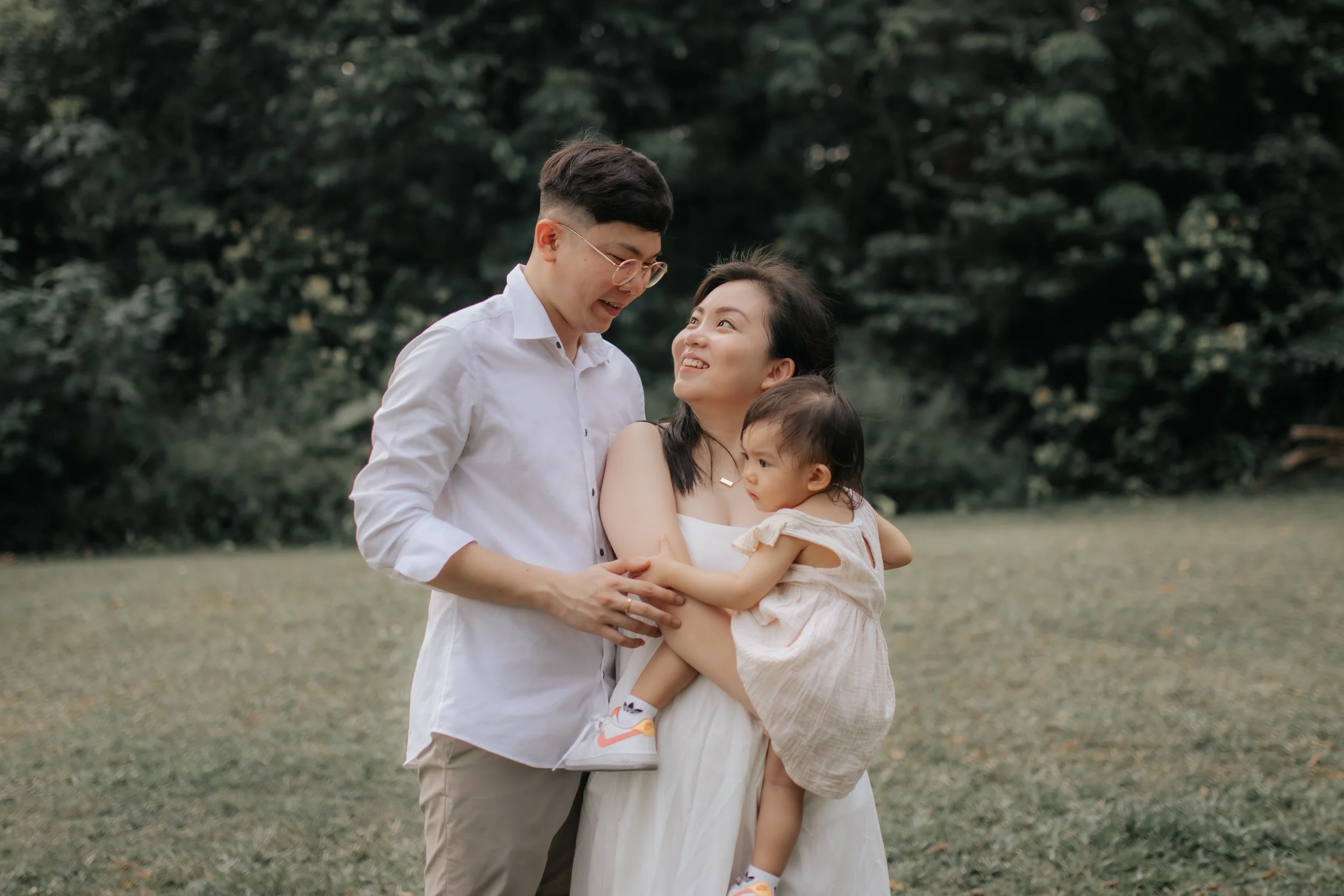 Light and airy family photo of a young family posing on a field of grass, captured in a soft outdoor setting in Singapore.