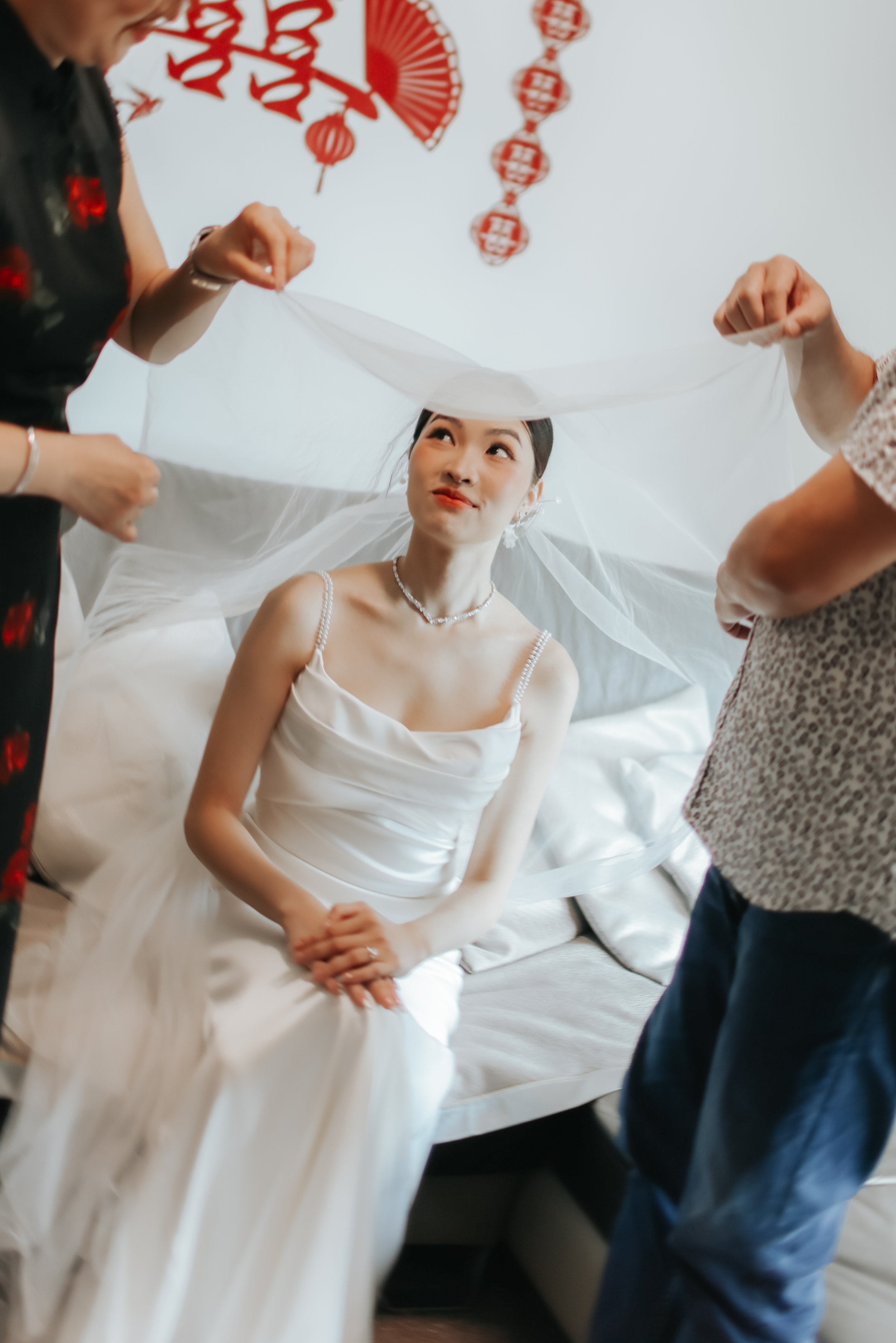 Light and airy actual day wedding photoshoot in Singapore, the bride is getting veiled by her parents at home in a touching and intimate moment. Captured by Arielle from Breadandbutterworks.
