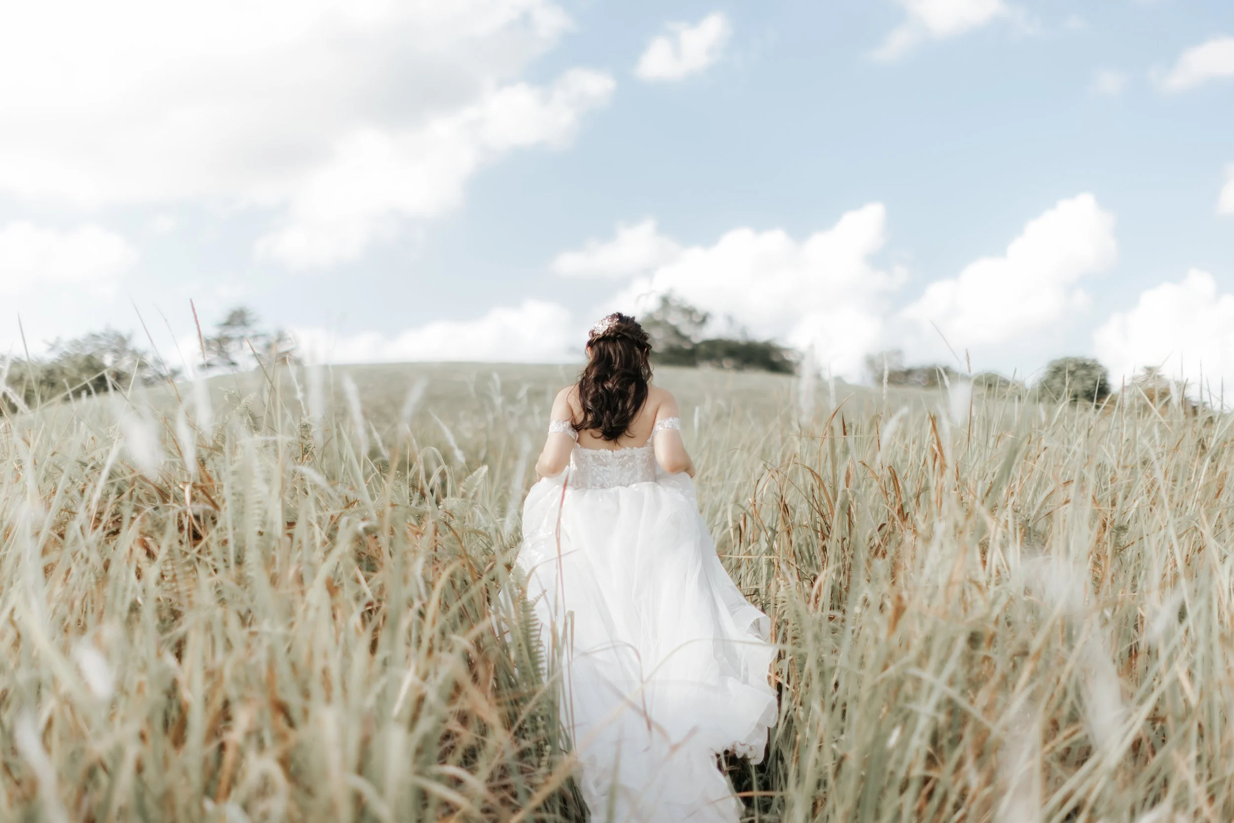 Light and airy pre-wedding photo of a bride walking through tall grass in an open field, captured in a soft outdoor setting in Singapore.