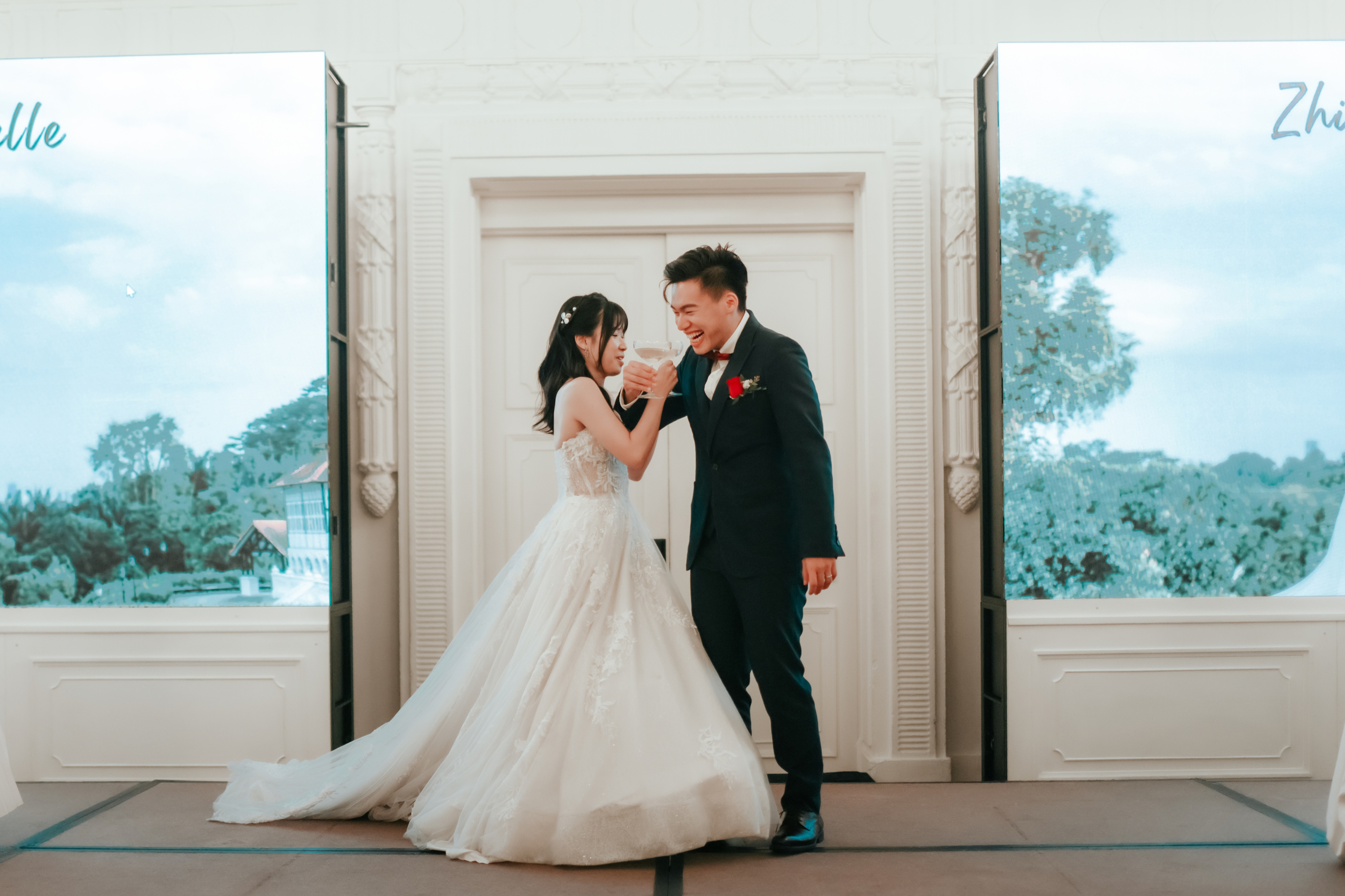 Light and airy actual day wedding photoshoot of the bride and groom linking arms and drinking champagne in The Fullerton Hotel in Singapore. Captured by Arielle for Breadandbutterworks.