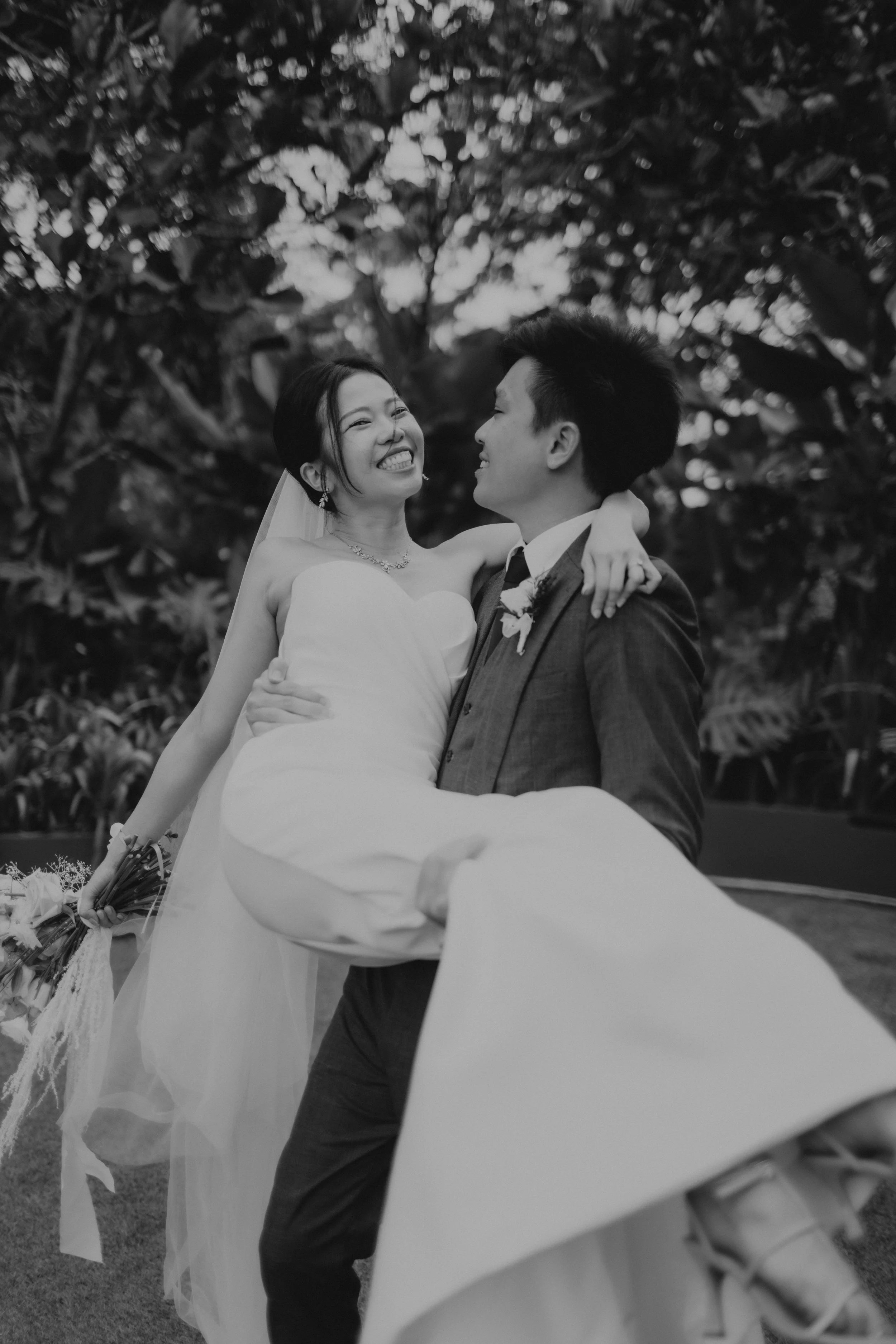 Cinematic black and white actual day wedding photoshoot of the groom carrying his wife romantically. Captured by Arielle for Breadandbutterworks.