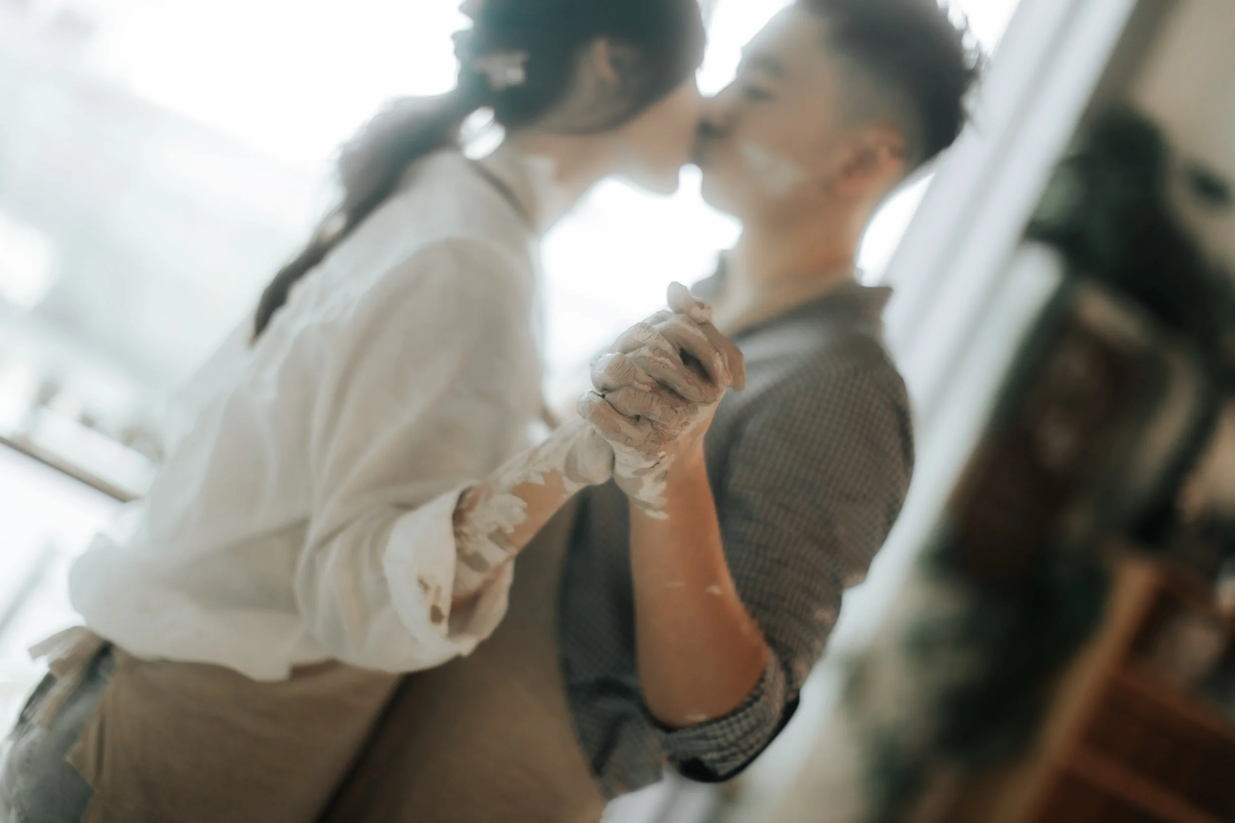 Intimate pre-wedding photoshoot at a pottery studio in Singapore (Tao Pottery), the couple share a dance and kiss in the studio. Captured in the light and airy style of Breadandbutterworks.