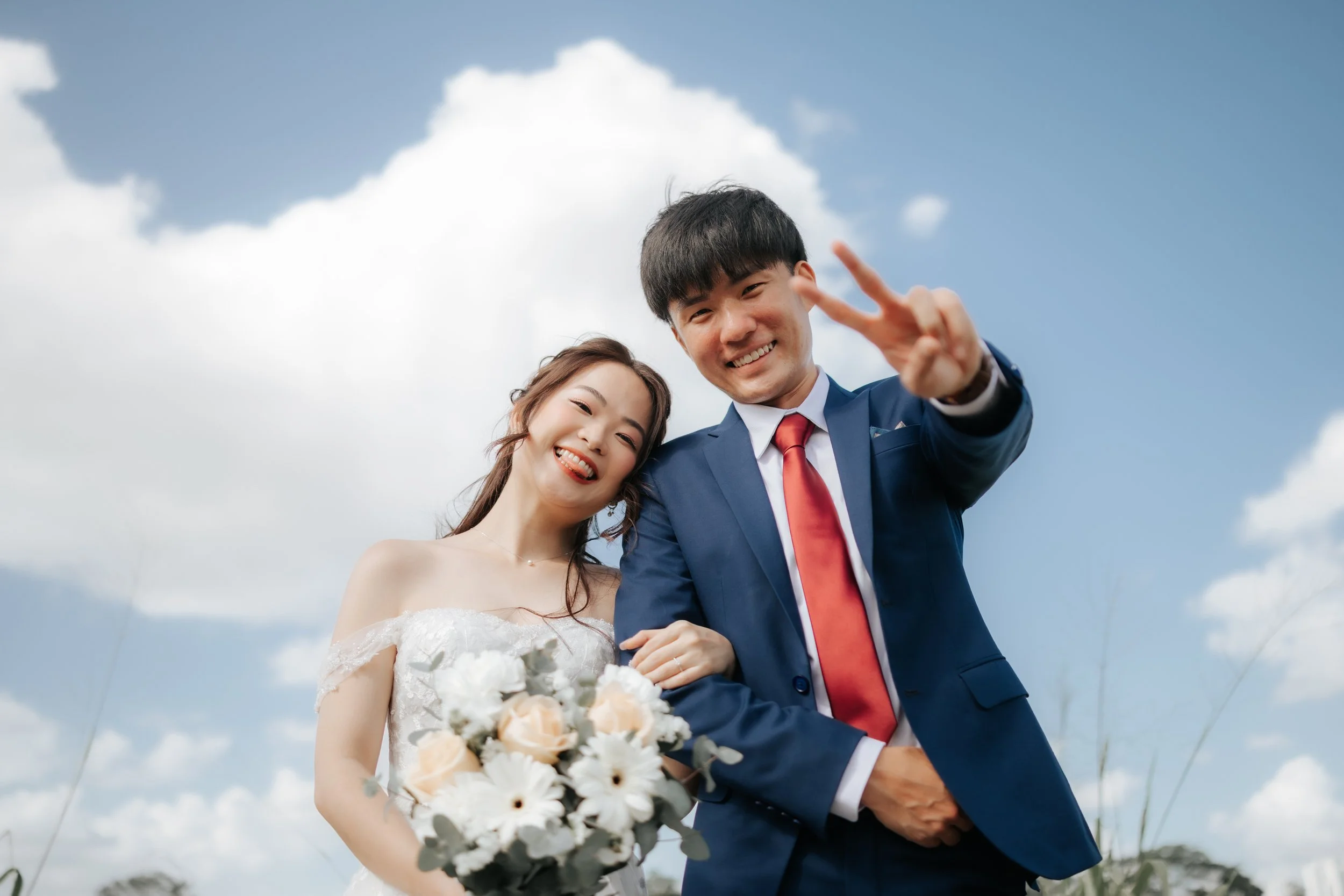 Romantic pre-wedding photo of a couple posing with blue skies and fluffy clouds in Jurong Lake Gardens in Singapore.