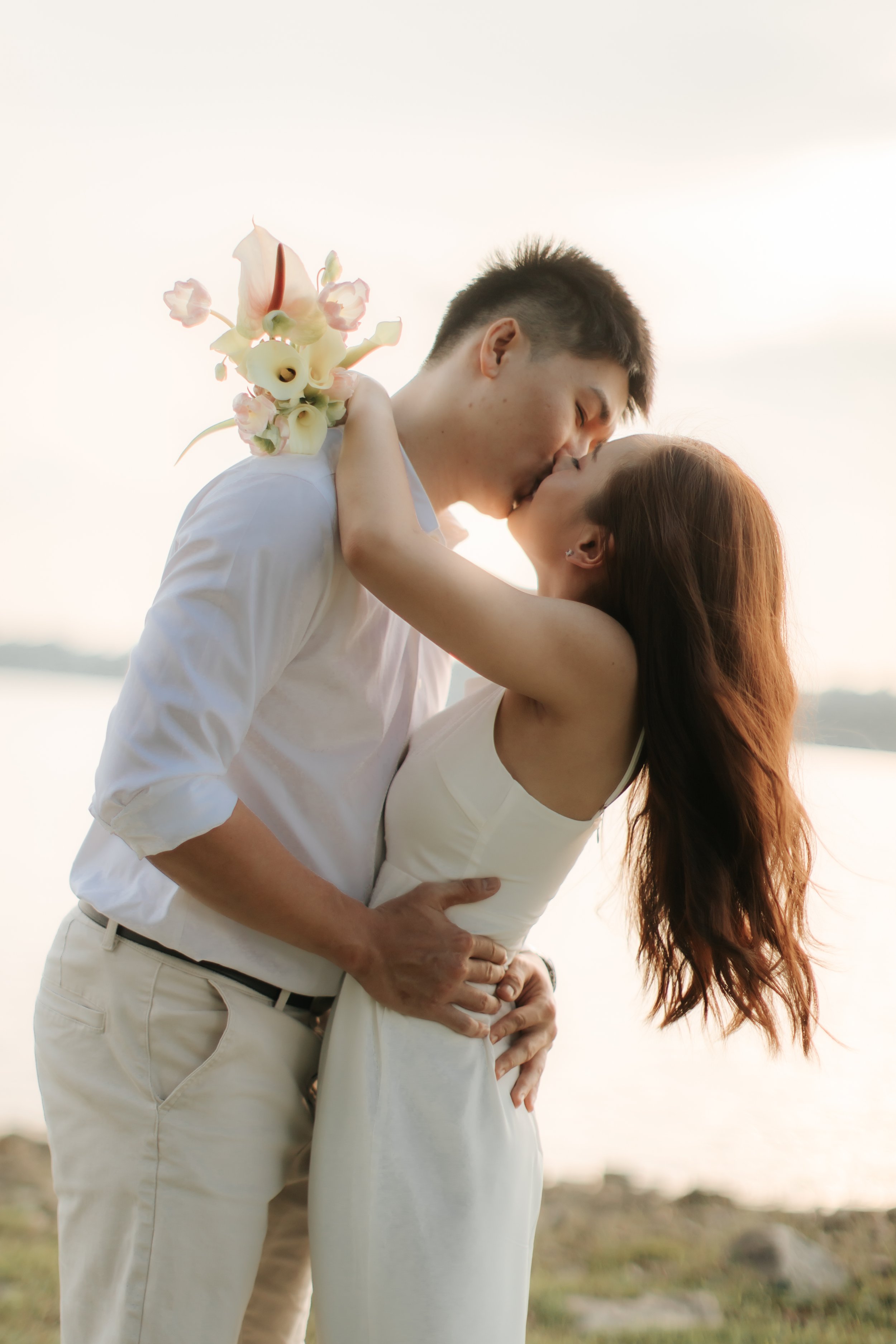 Romantic and airy pre-wedding photoshoot at Upper Seletar Reservoir, the couple is sharing a kiss with the sunset as a backdrop. Captured by Arielle from Breadandbutterworks.