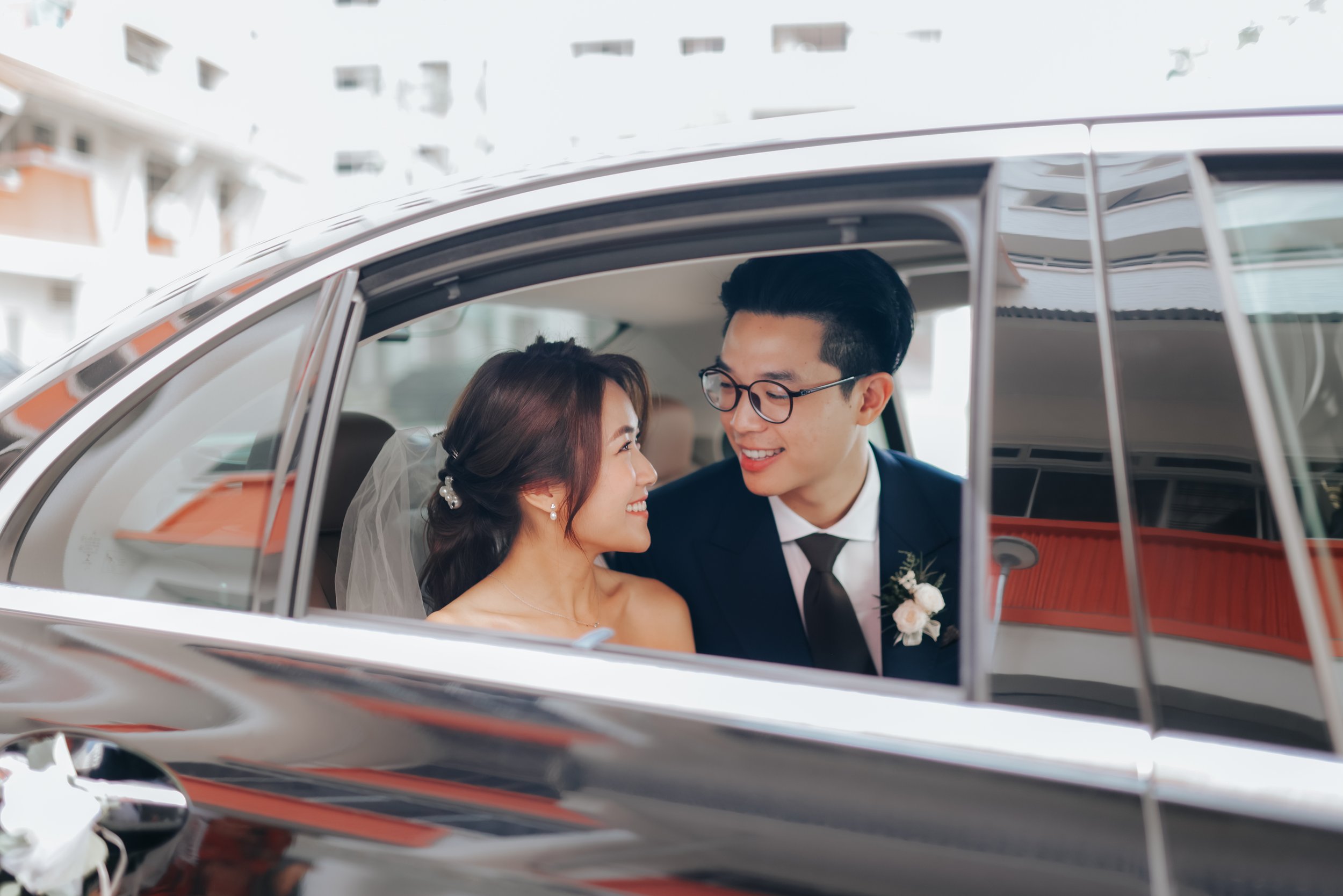 Light and airy actual day wedding photography in Singapore, the bride and groom are smiling lovingly at each other in their matrimonial car. Captured by Ash for Breadandbutterworks.