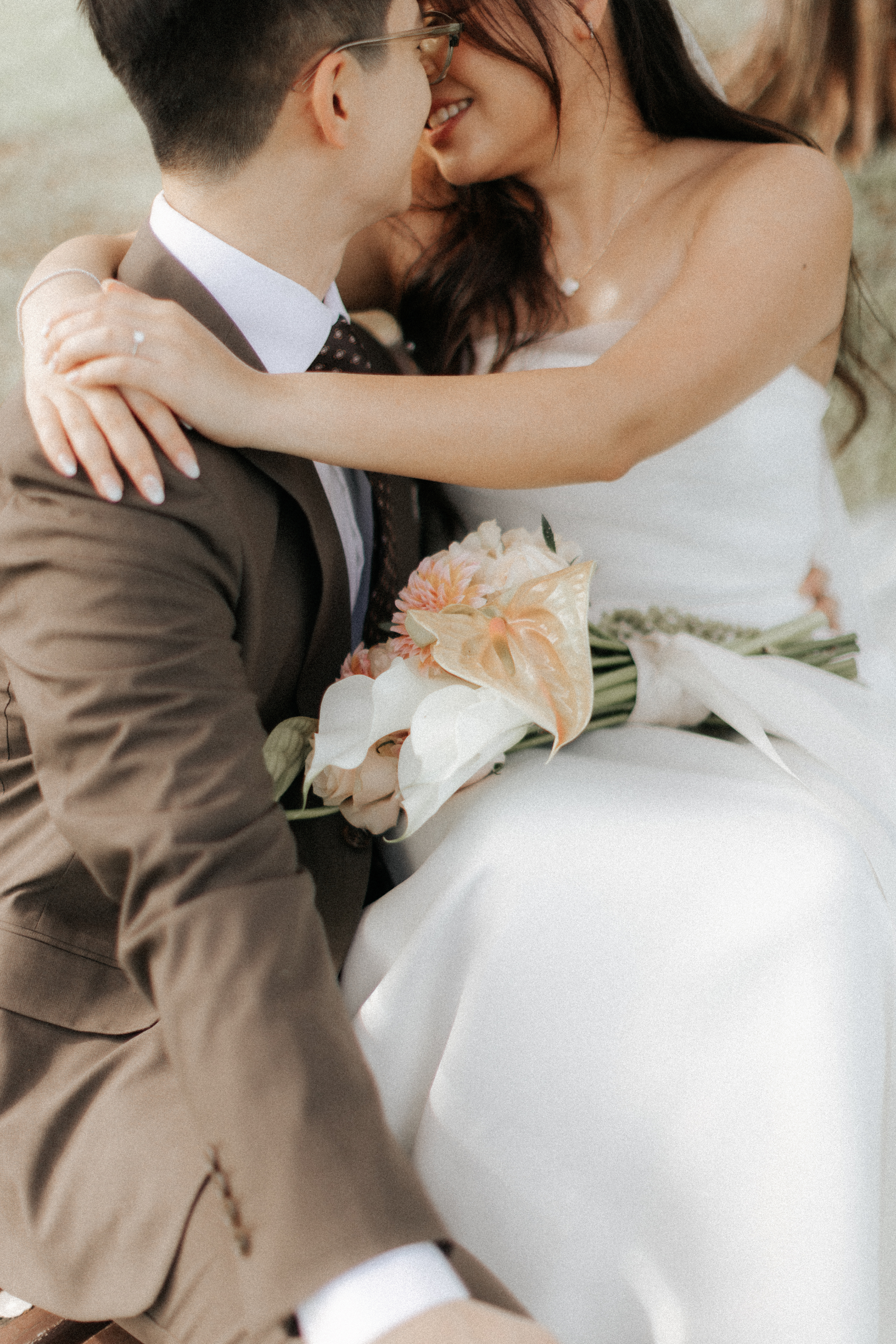 Intimate actual day wedding photo of a couple sharing a close moment with a bridal bouquet, captured by Ash for Breadandbutterworks in a soft and heartfelt style.
