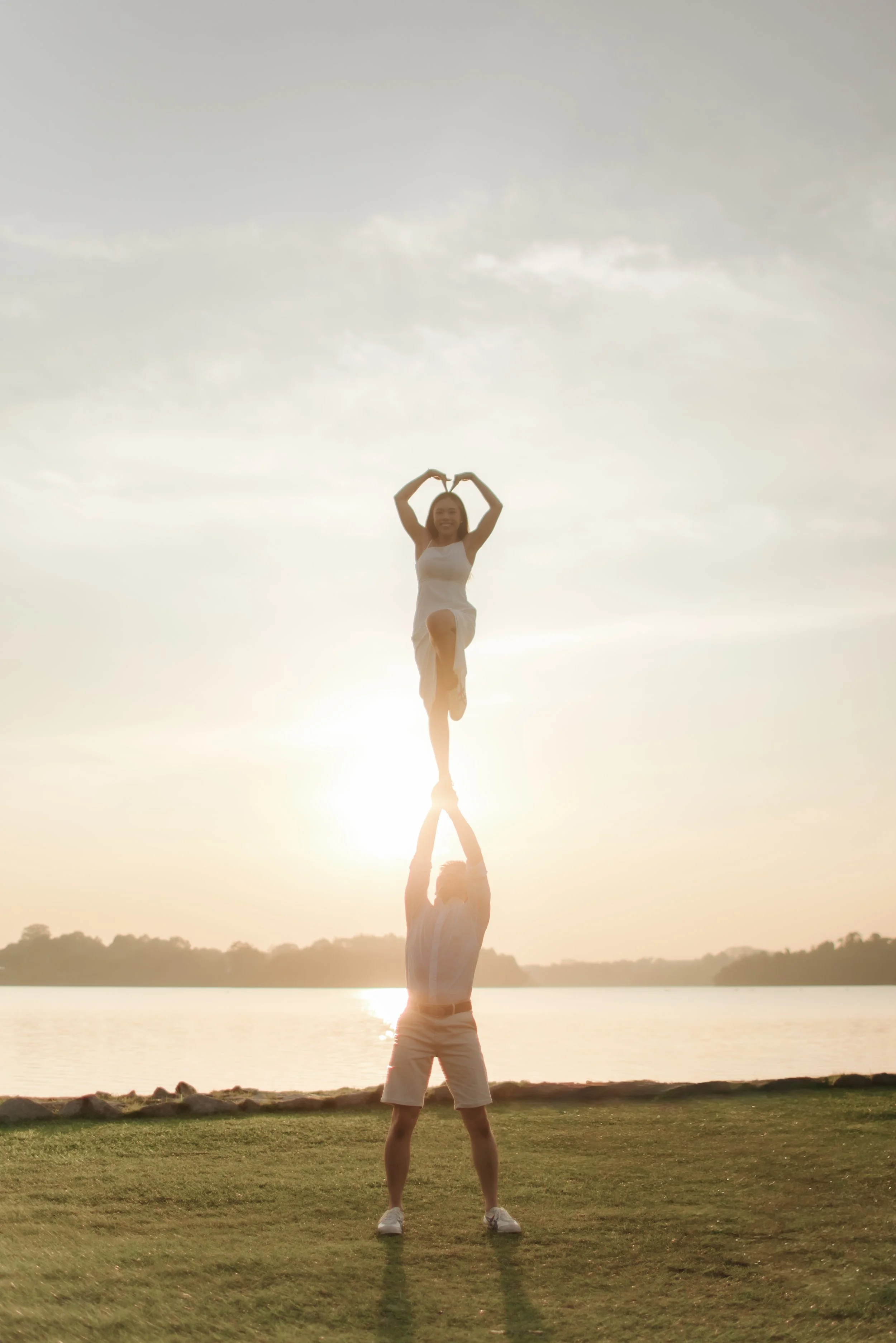 Romantic and airy pre-wedding photoshoot at Upper Seletar Reservoir, the couple is performing a cheerleading routine with the sunset in the background. Captured by Arielle from Breadandbutterworks.