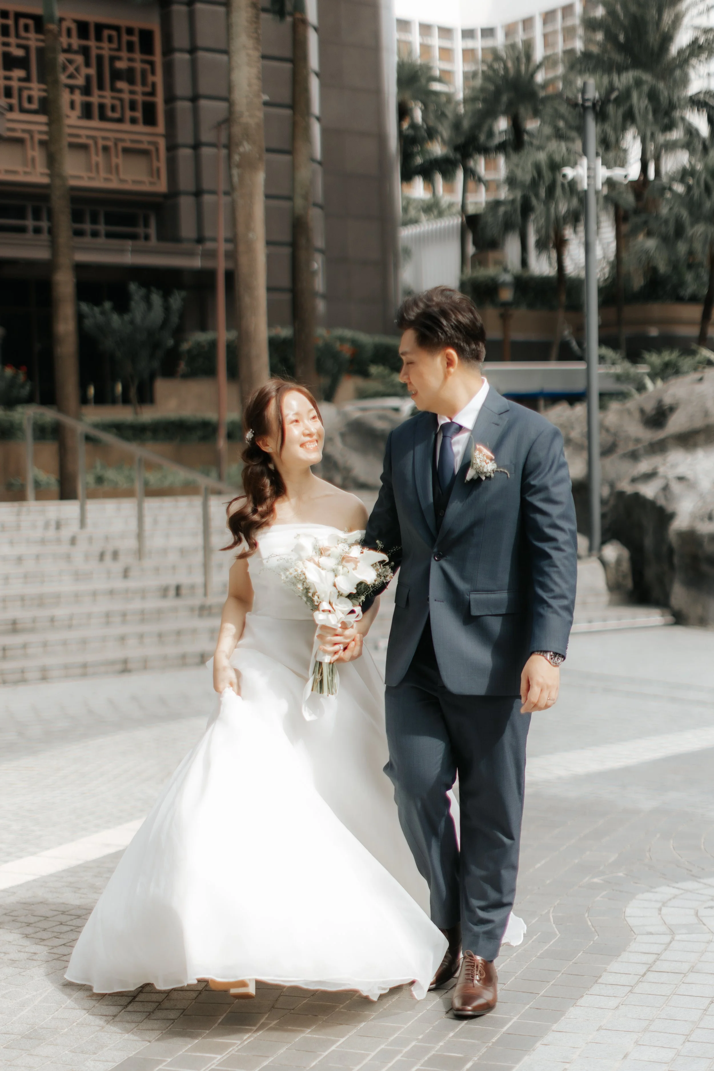 Joyful actual day wedding photoshoot of a couple walking along a street in Singapore towards their car, captured by Breadandbutterworks in a soft and heartfelt style.