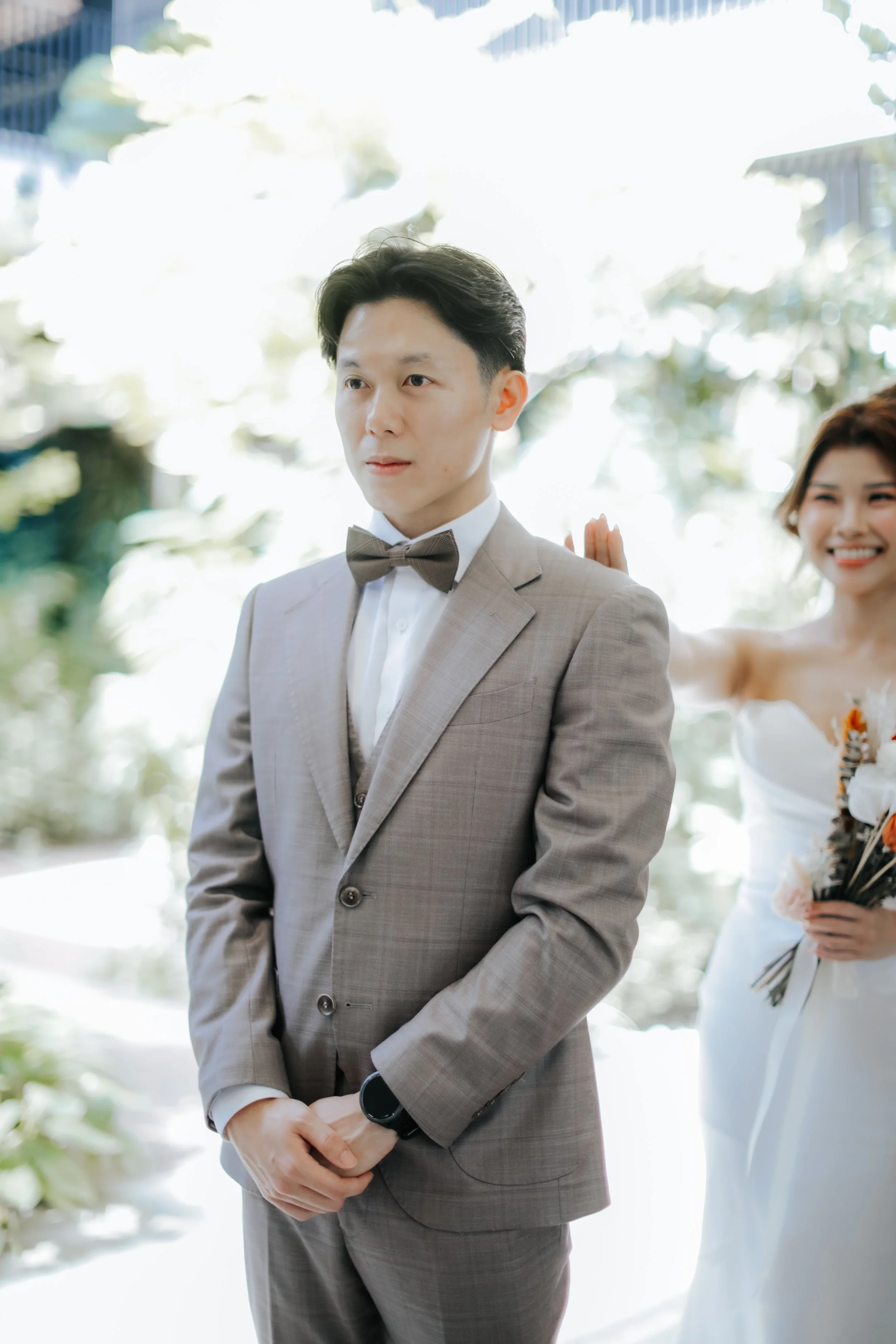 Light and airy actual day wedding photoshoot at Canopy HortPark, the bride is about to tap the groom on the shoulder for him to get his first look. Captured by Arielle from Breadandbutterworks.