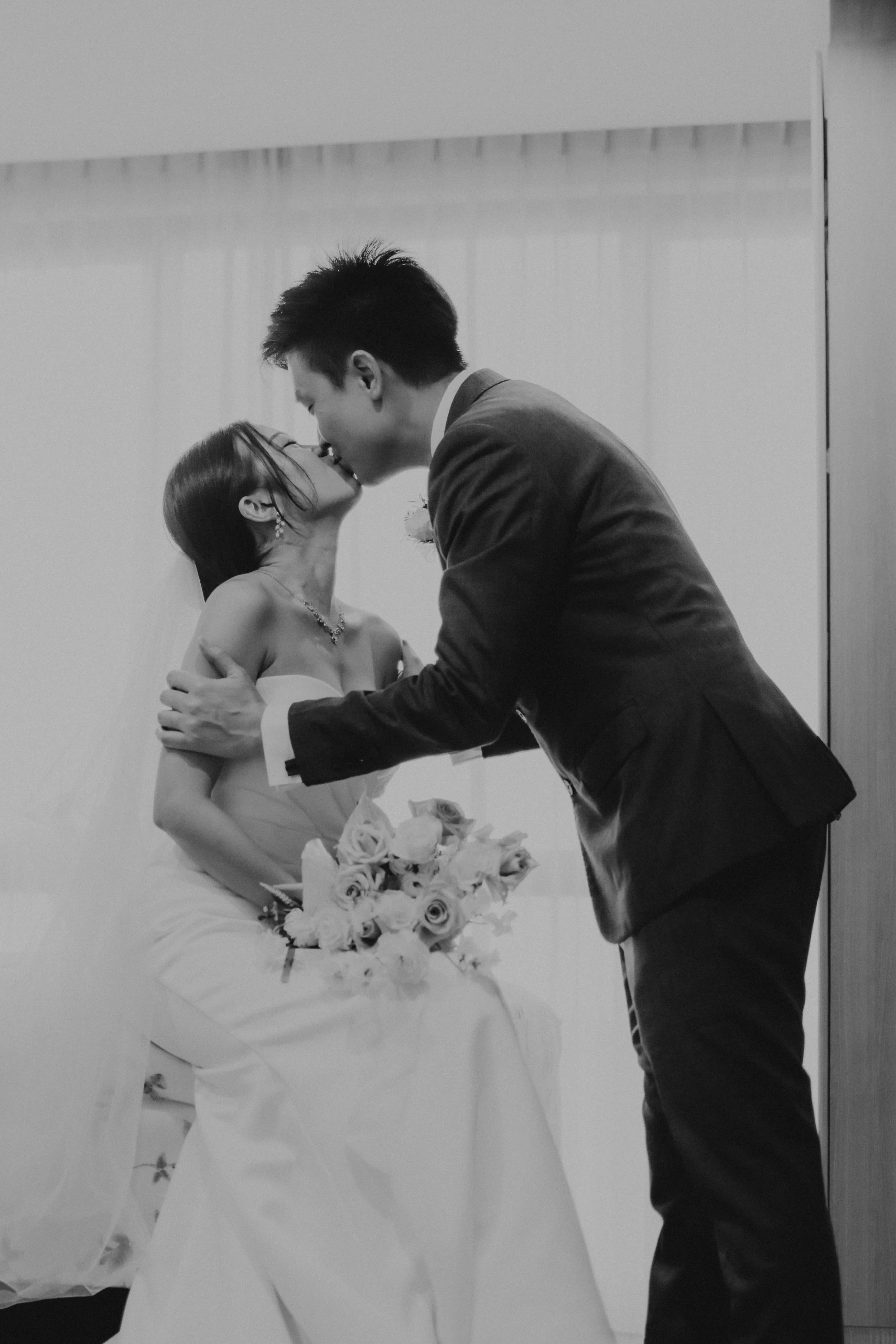 Cinematic black and white actual day wedding photoshoot of the groom's first look at his bride and sharing a kiss. Captured by Arielle for Breadandbutterworks.