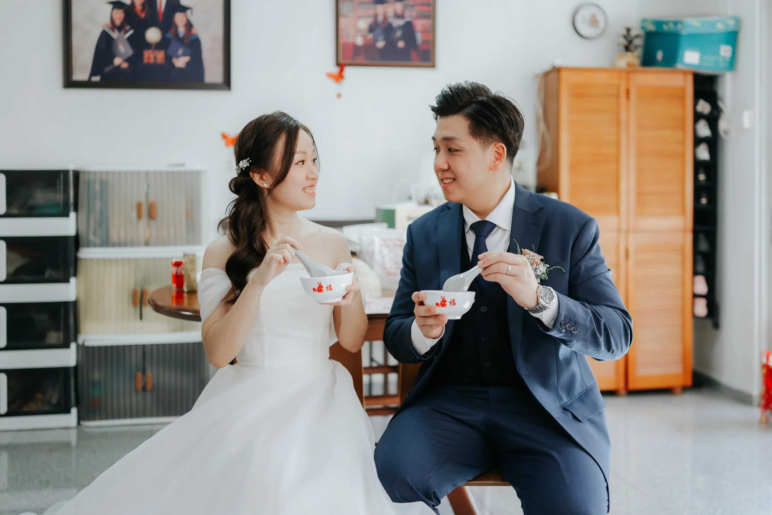 Joyful actual day wedding photoshoot of a couple eating their traditional tang yuan together at home, captured by Breadandbutterworks in a soft and heartfelt style.