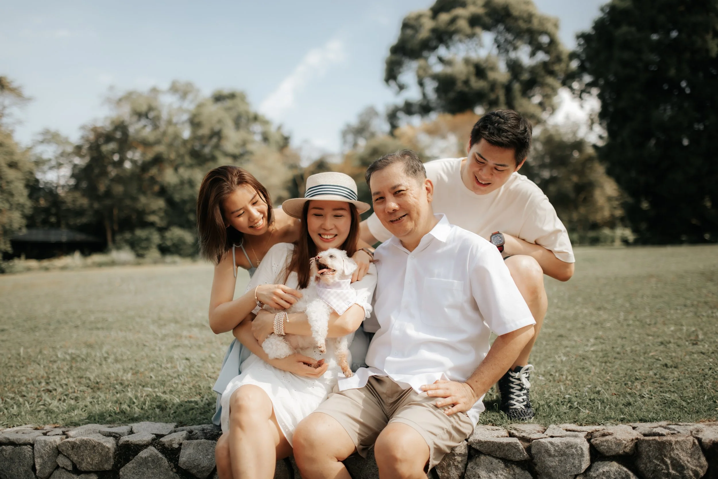 Light and airy family photoshoot in Singapore featuring a family sitting outdoors with their pet dog, captured by Breadandbutterworks.