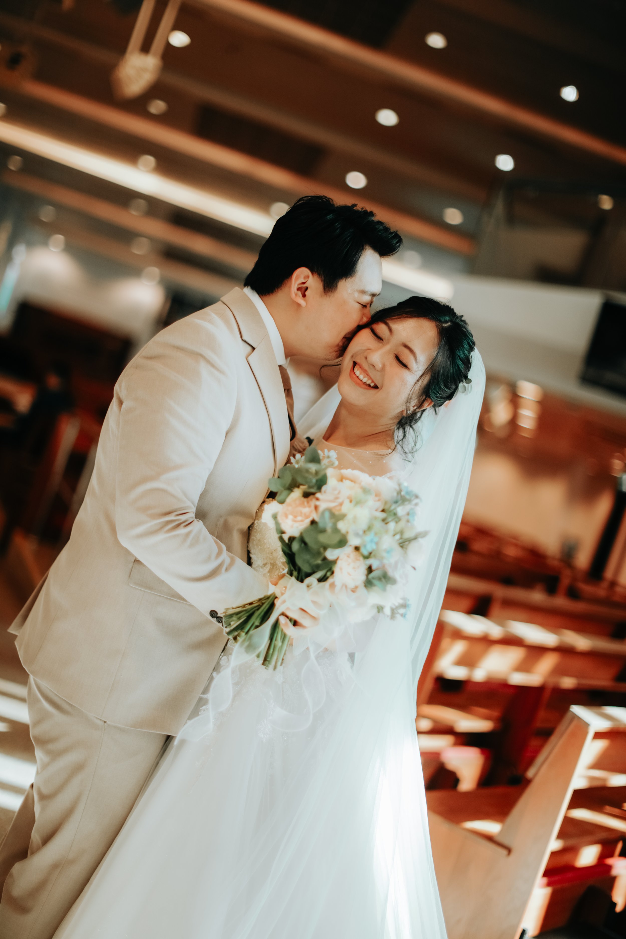 Light and airy intimate actual day wedding photoshoot taken in a Catholic Church of the couple posing and kissing. Captured by Arielle for Breadandbutterworks. 