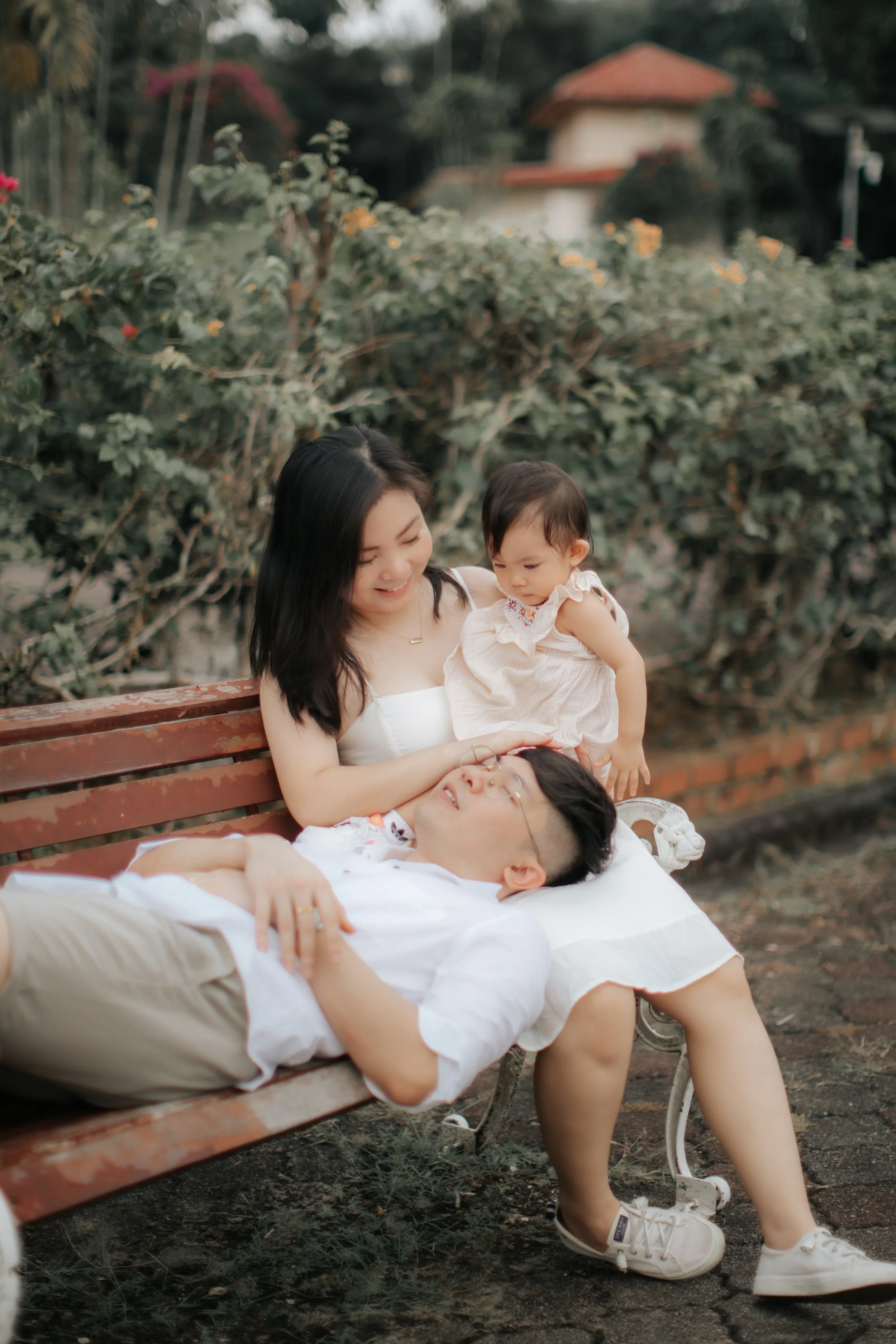 Light and airy family photo of a young family relaxing on a bench, captured in a soft outdoor setting in Singapore.