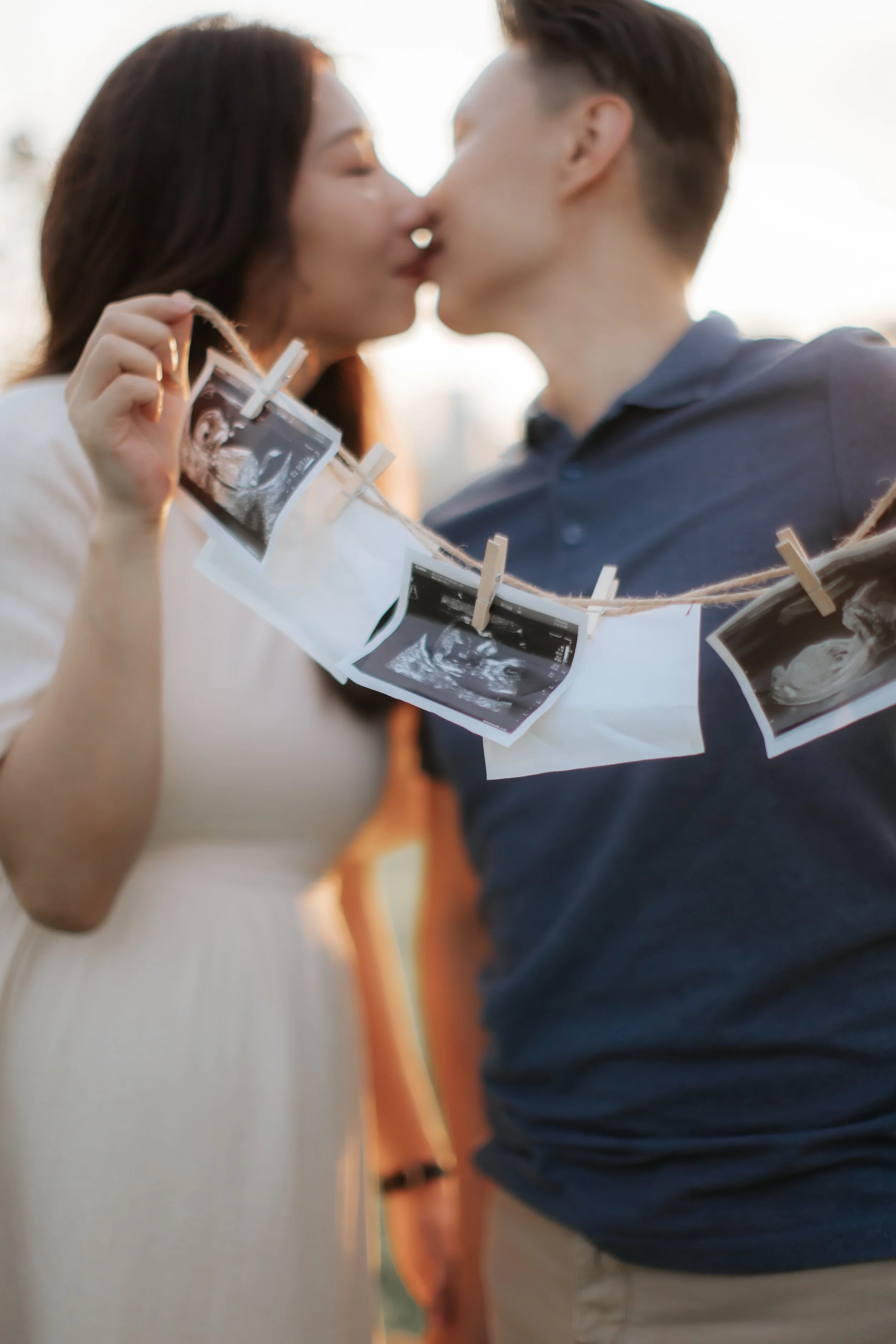 A couple poses for their maternity shoot while sharing a kiss during golden hour in Singapore, captured by Breadandbutterworks in a soft and heartfelt style.