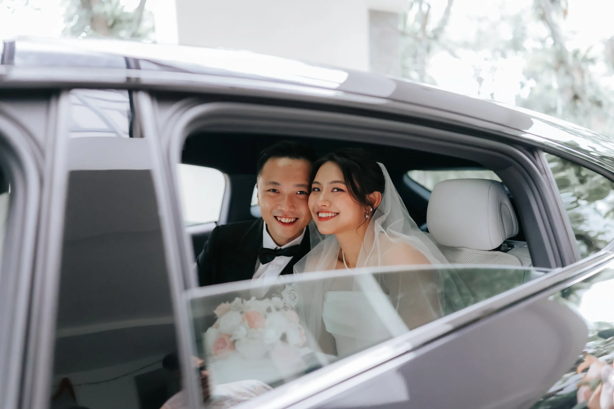 Joyful actual day wedding photography of the couple posing in their bridal car, captured by Breadandbutterworks in a soft and heartfelt style.