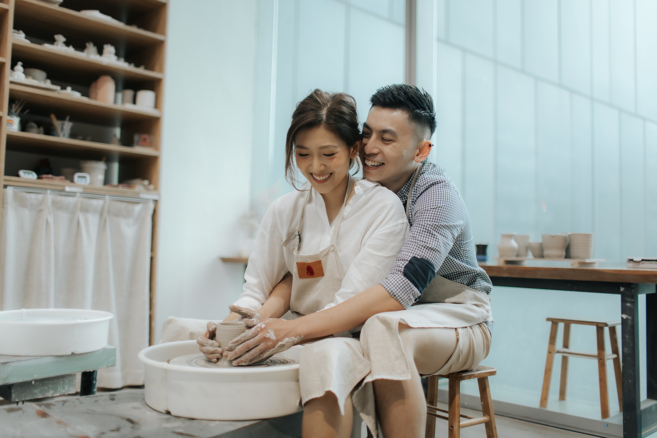 Intimate pre-wedding photoshoot at a pottery studio in Singapore (Tao Pottery), the couple is working on a pottery wheel in a romantic fashion. Captured in the light and airy style of Breadandbutterworks.