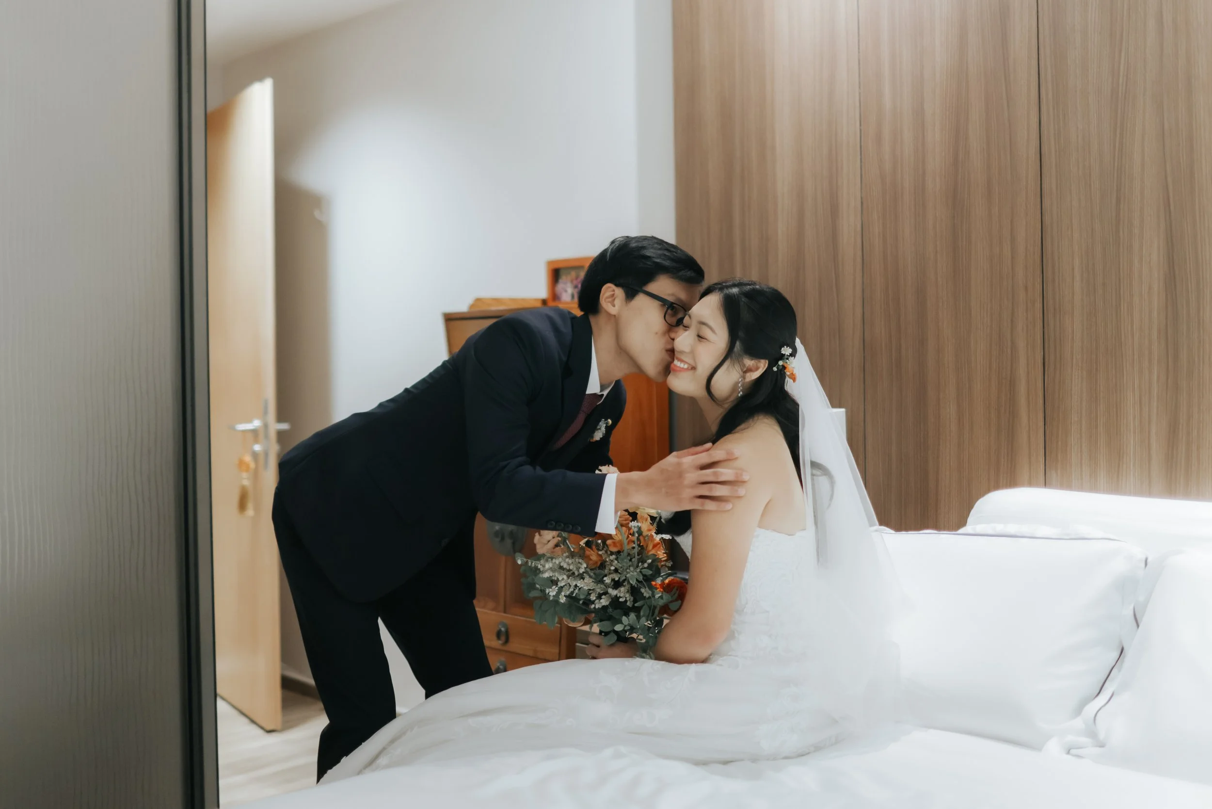 Actual day wedding photoshoot of the couple's first look at each other, the groom lovingly kisses the bride on the cheek. Captured in a light and airy style by Arielle for Breadandbutterworks.