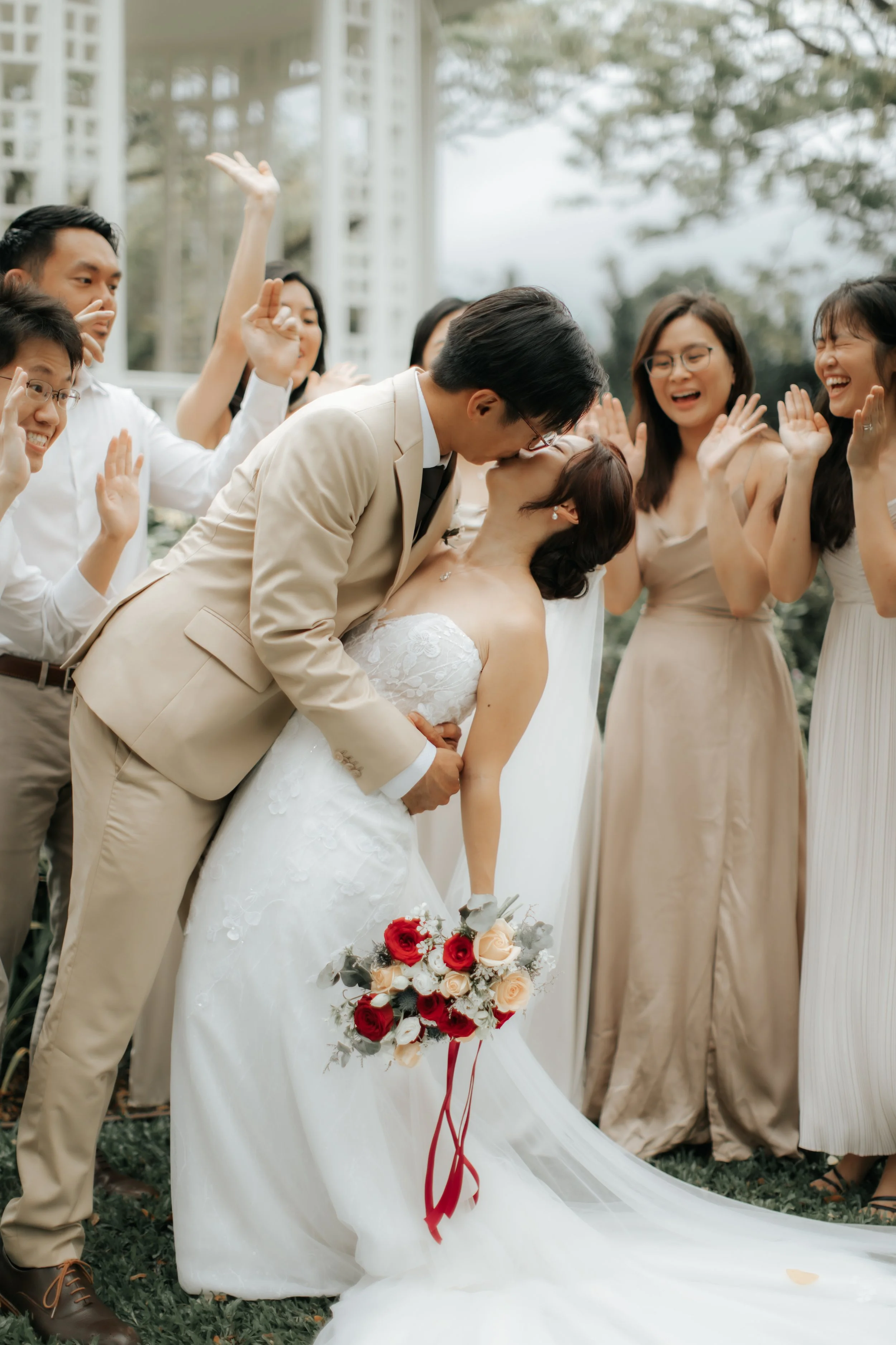 Light and airy actual day wedding photoshoot at The Villa in Singapore of the couple sharing a cinematic kiss among their friends. Captured by Arielle for Breadandbutterworks.