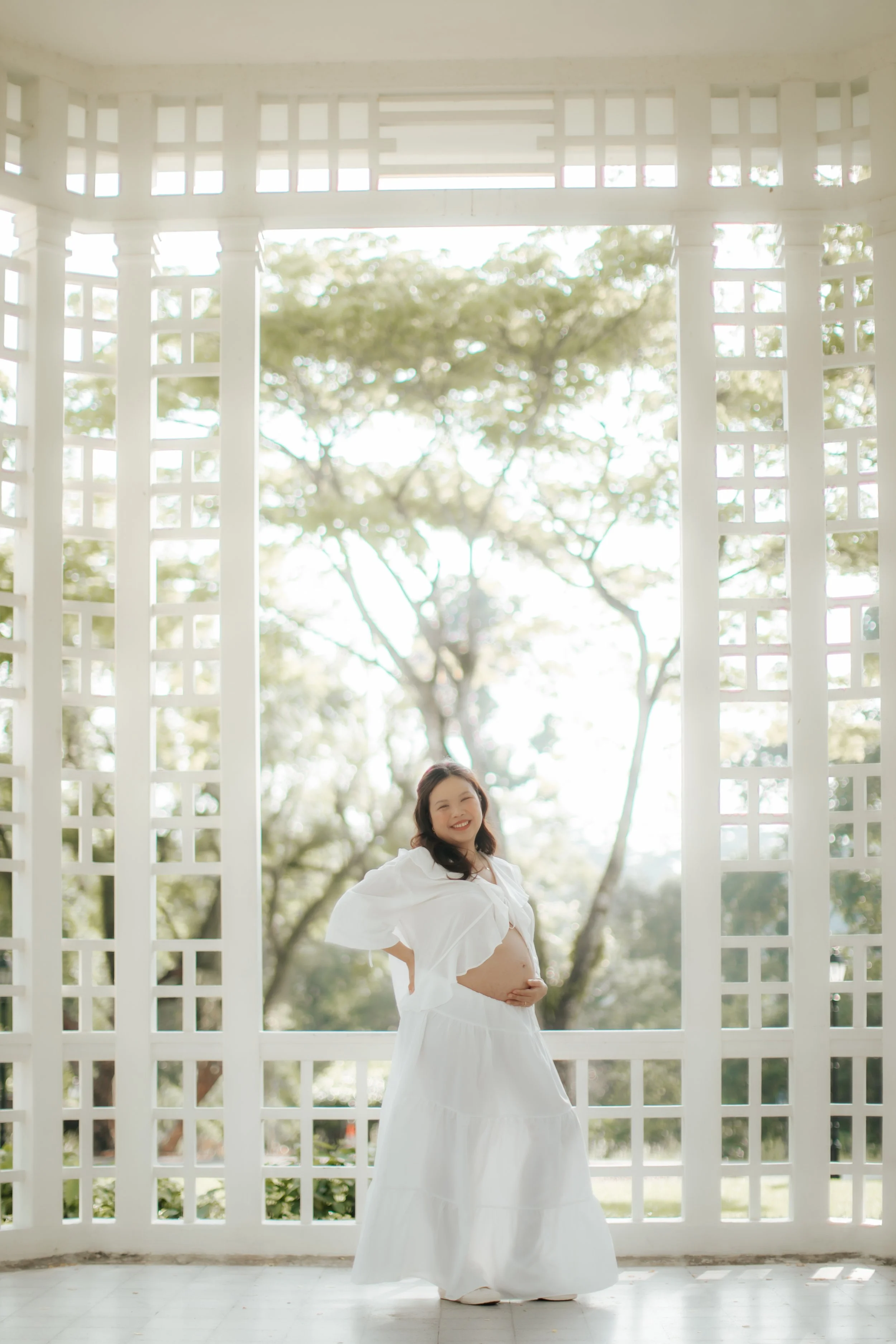 Light and airy maternity shoot at bandstand, the mother-to-be poses cheerfully, captured by Arielle for Breadandbutterworks.
