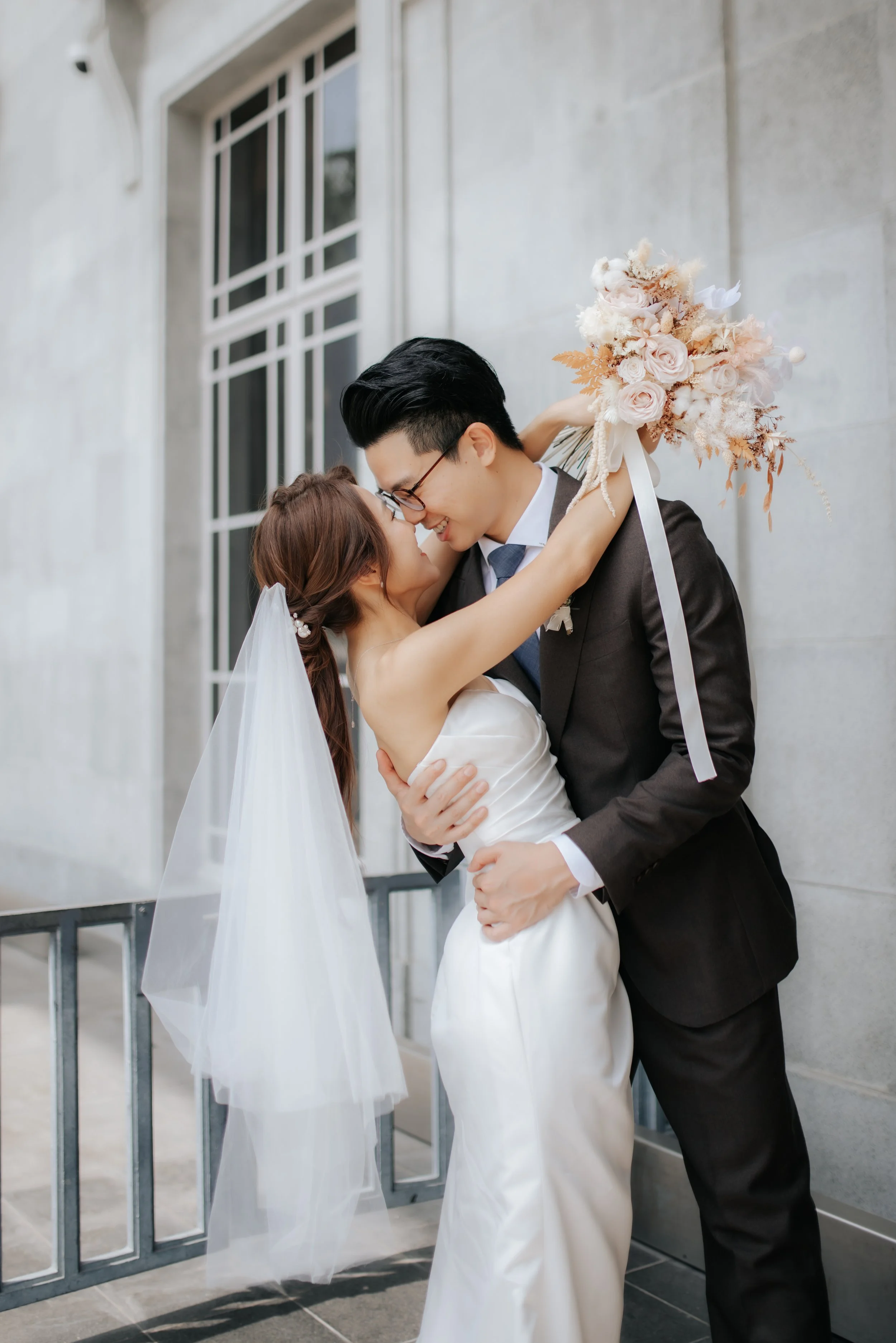 Light and airy actual day wedding photography at Sky Garden Sentosa in Singapore, the couple share a romantic kiss by the doorway captured by Ash for Breadandbutterworks.