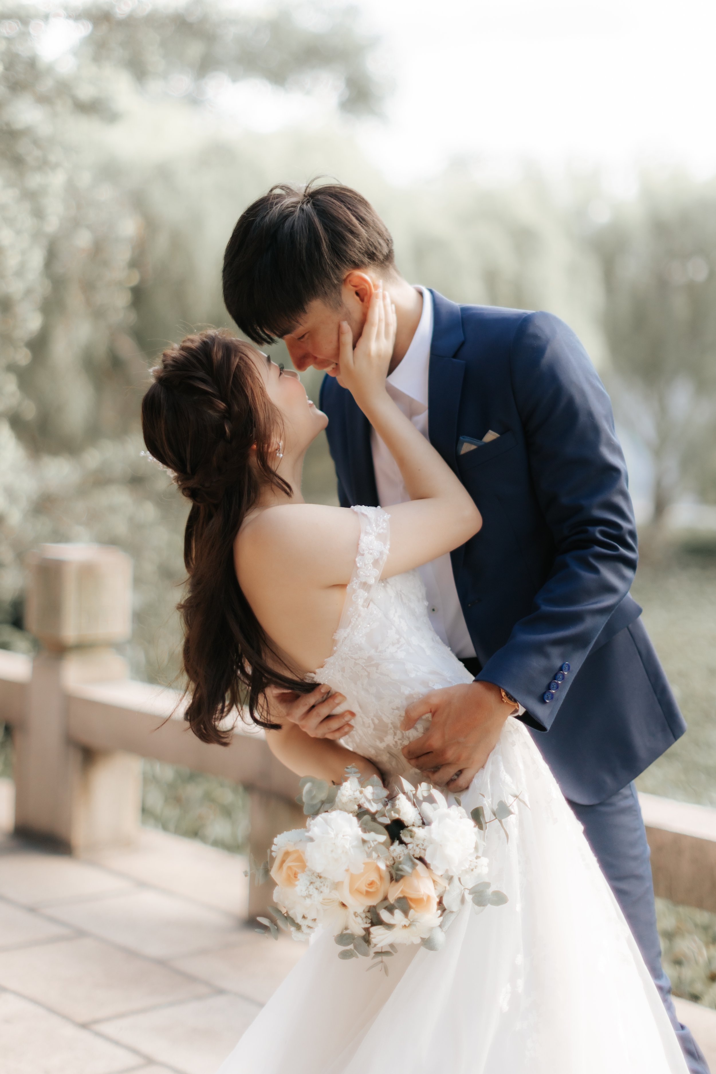 Romantic pre-wedding photo of a couple sharing a kiss, with the groom dipping the bride against a soft outdoor garden backdrop in Singapore.