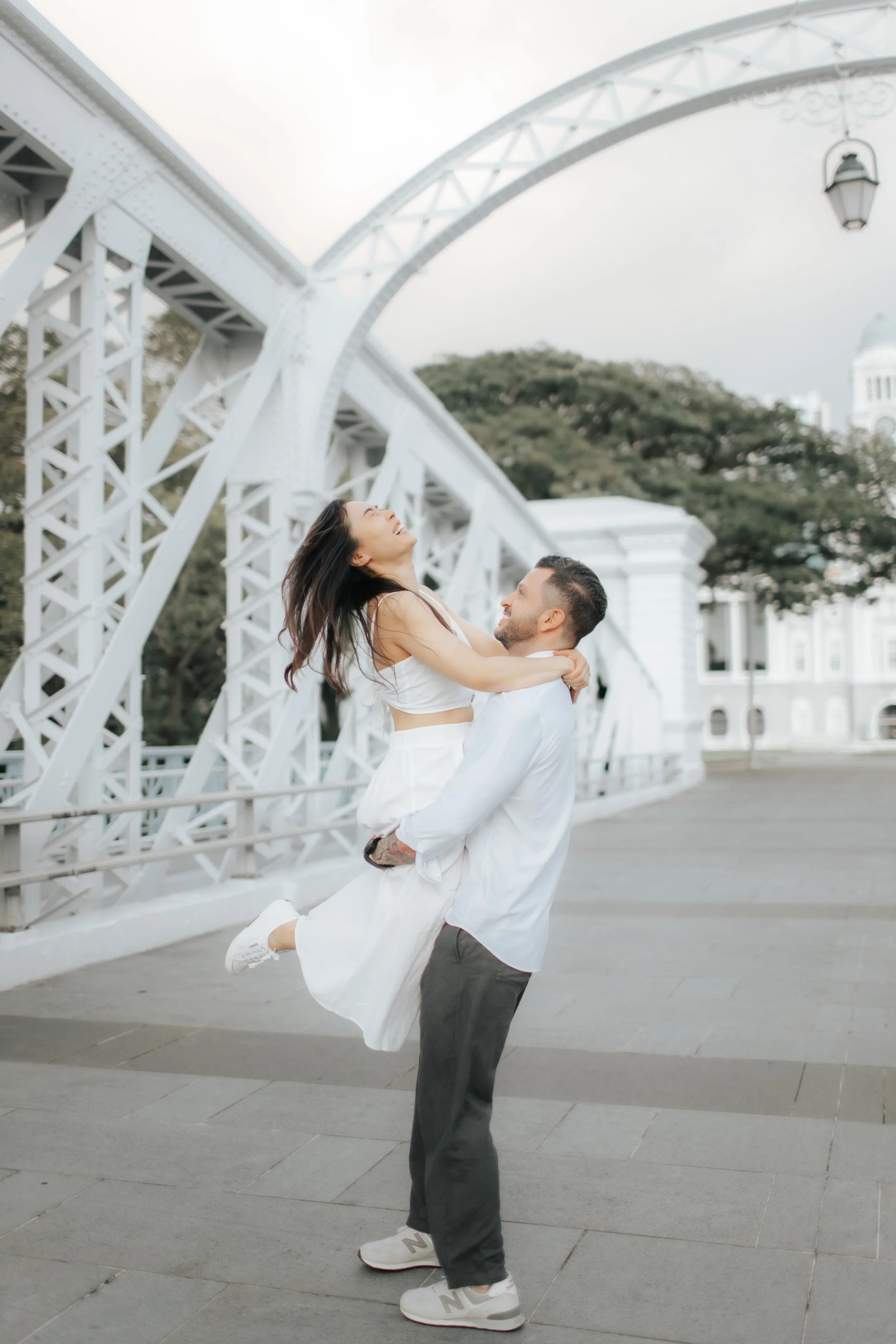 Light and airy proposal photoshoot at Anderson Bridge, the bride-to-be leaps into her fiance's arms as his lifts her off her feet. Captured by Arielle for Breadandbutterworks.