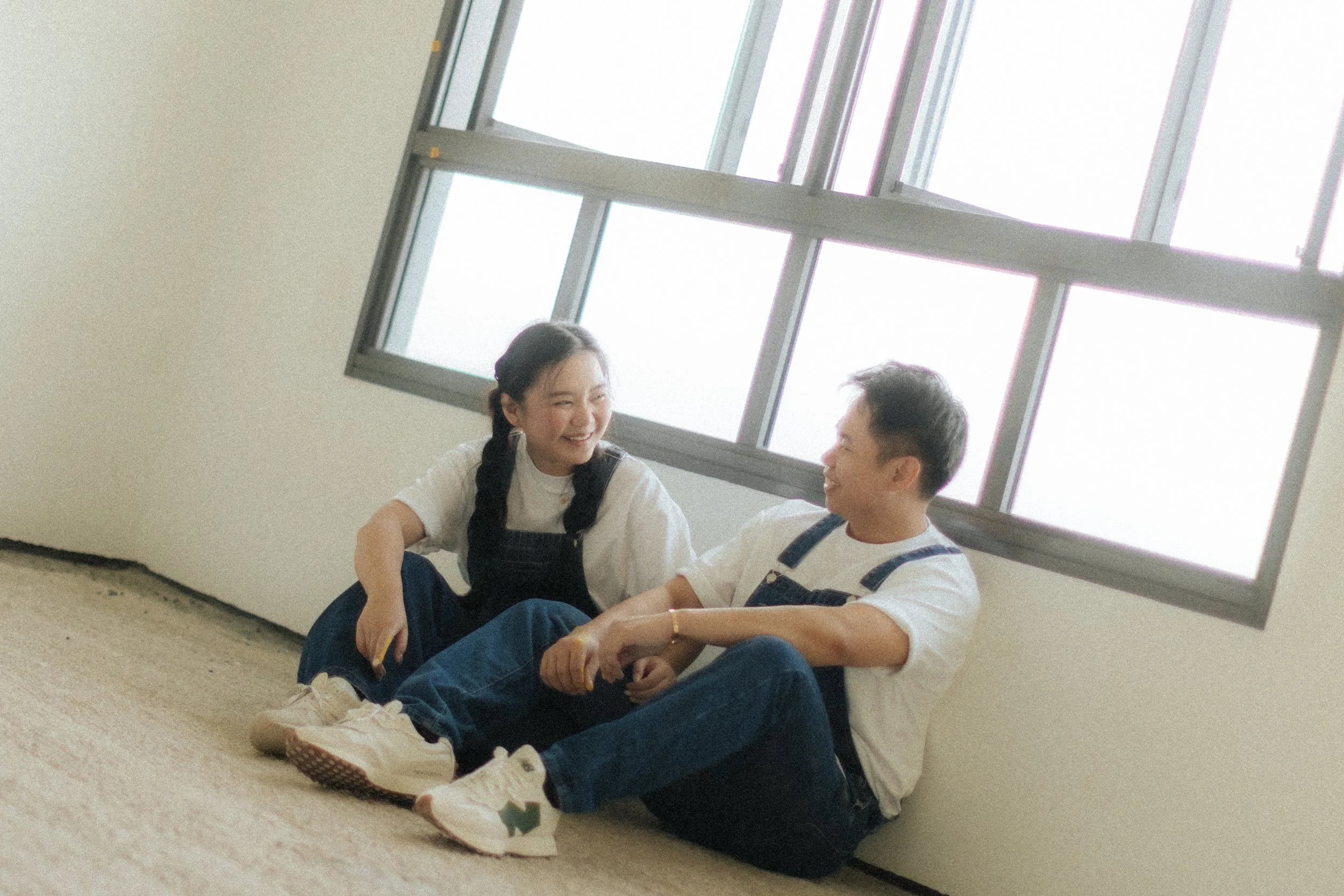 Playful home pre-wedding photo of a couple painting their marital home together, in this photo they are taking a break and happily having a conversation. Captured by Breadandbutterworks in a light, airy and heartfelt style.