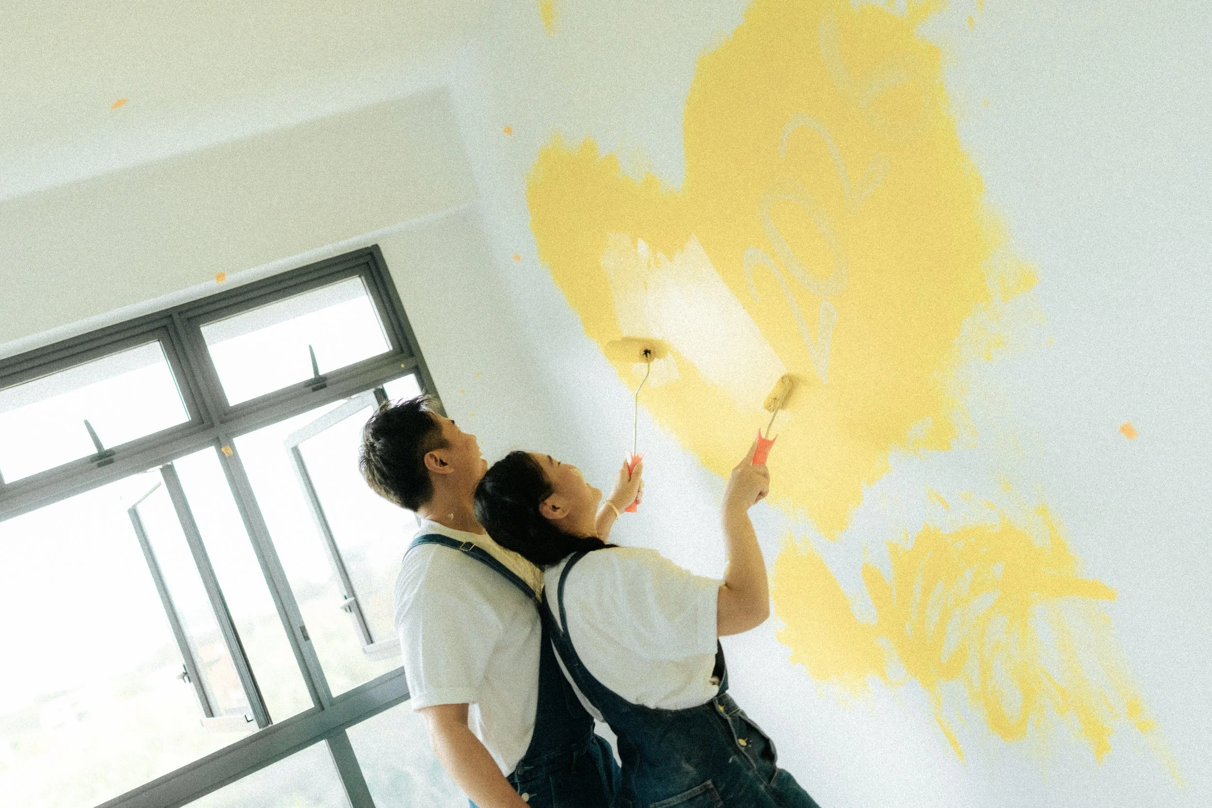 Playful home pre-wedding photo of a couple painting their marital home together, captured by Breadandbutterworks in a light, airy and heartfelt style.