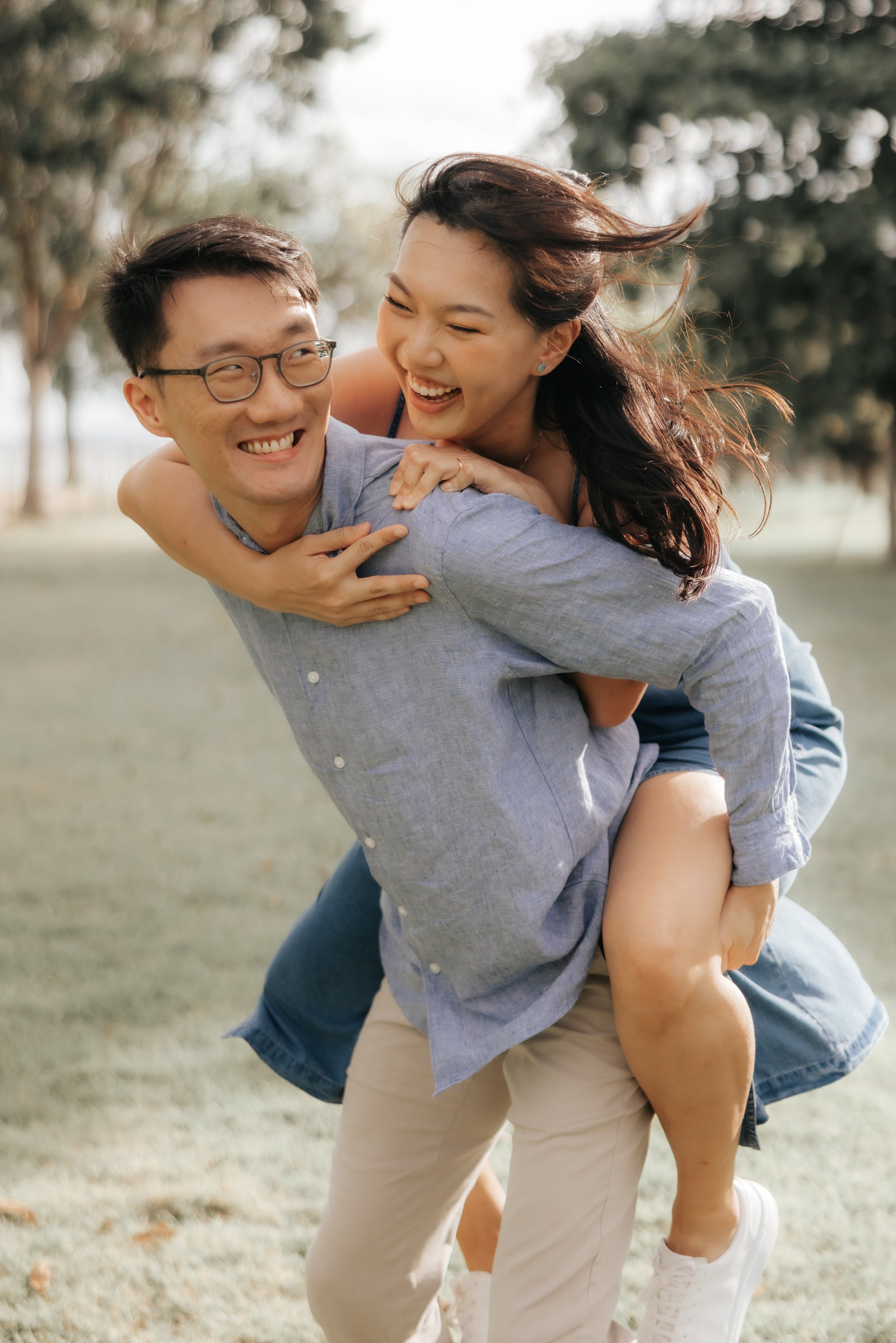 Playful pre-wedding photo of a couple piggy-backing at East Coast Park, captured by Breadandbutterworks in a soft and heartfelt style.