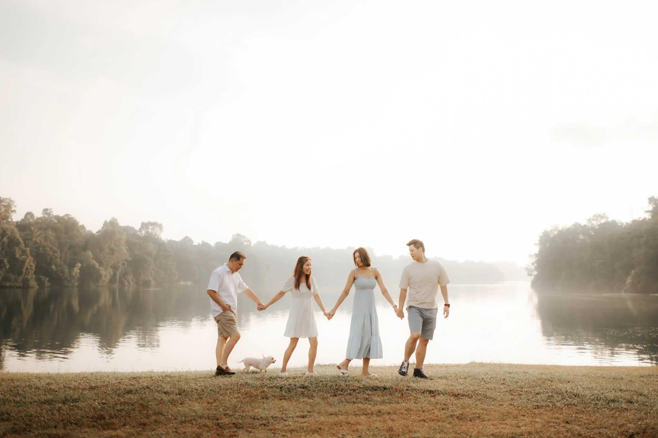 Light and airy family photoshoot in Singapore featuring a family strolling through a park outdoors with their pet dog, captured by Breadandbutterworks.